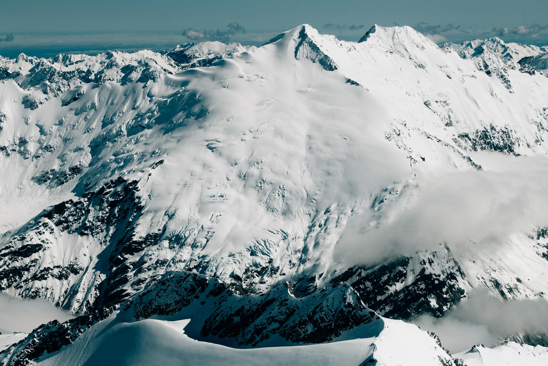 Aerial of a broad snowfield and ridgelines under thin cloud