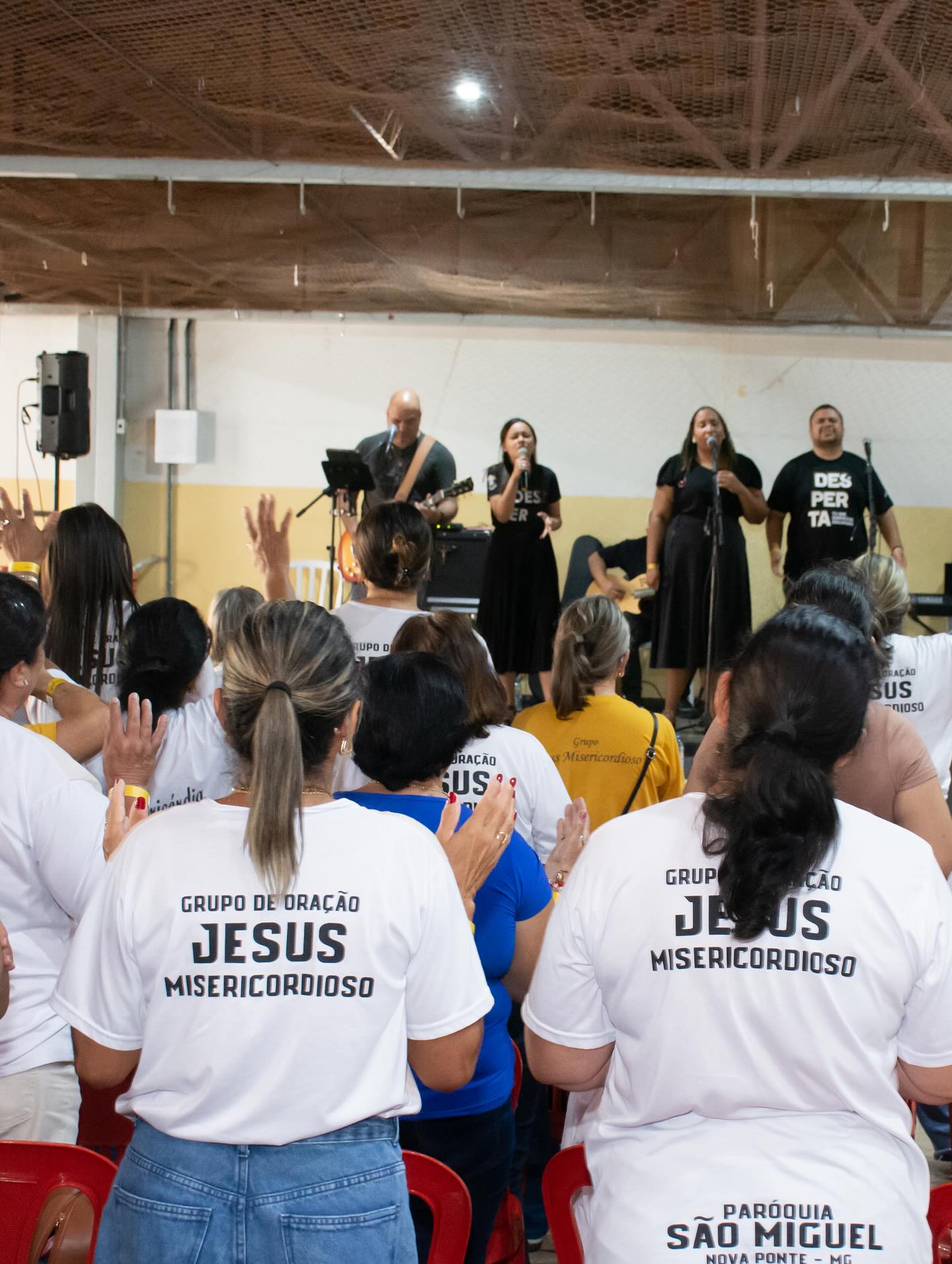 Confident male speaker in a white shirt and headset mic gesticulates on stage with teal spotlighting.