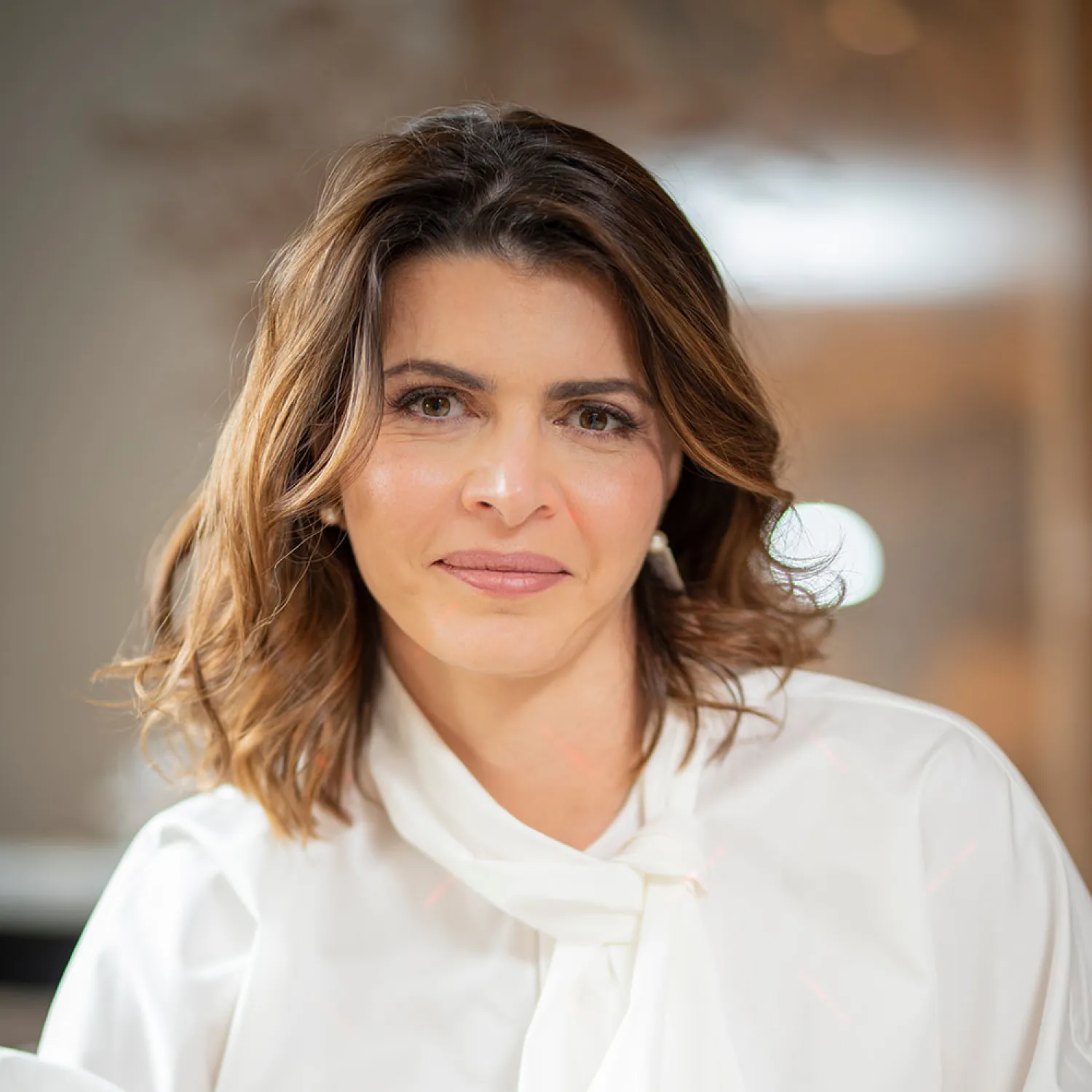 A young person with curly hair smiles at the camera while sitting in front of a laptop against a dark background.