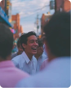 Smiling young man in a white shirt laughing heartily with friends in a vibrant outdoor street setting