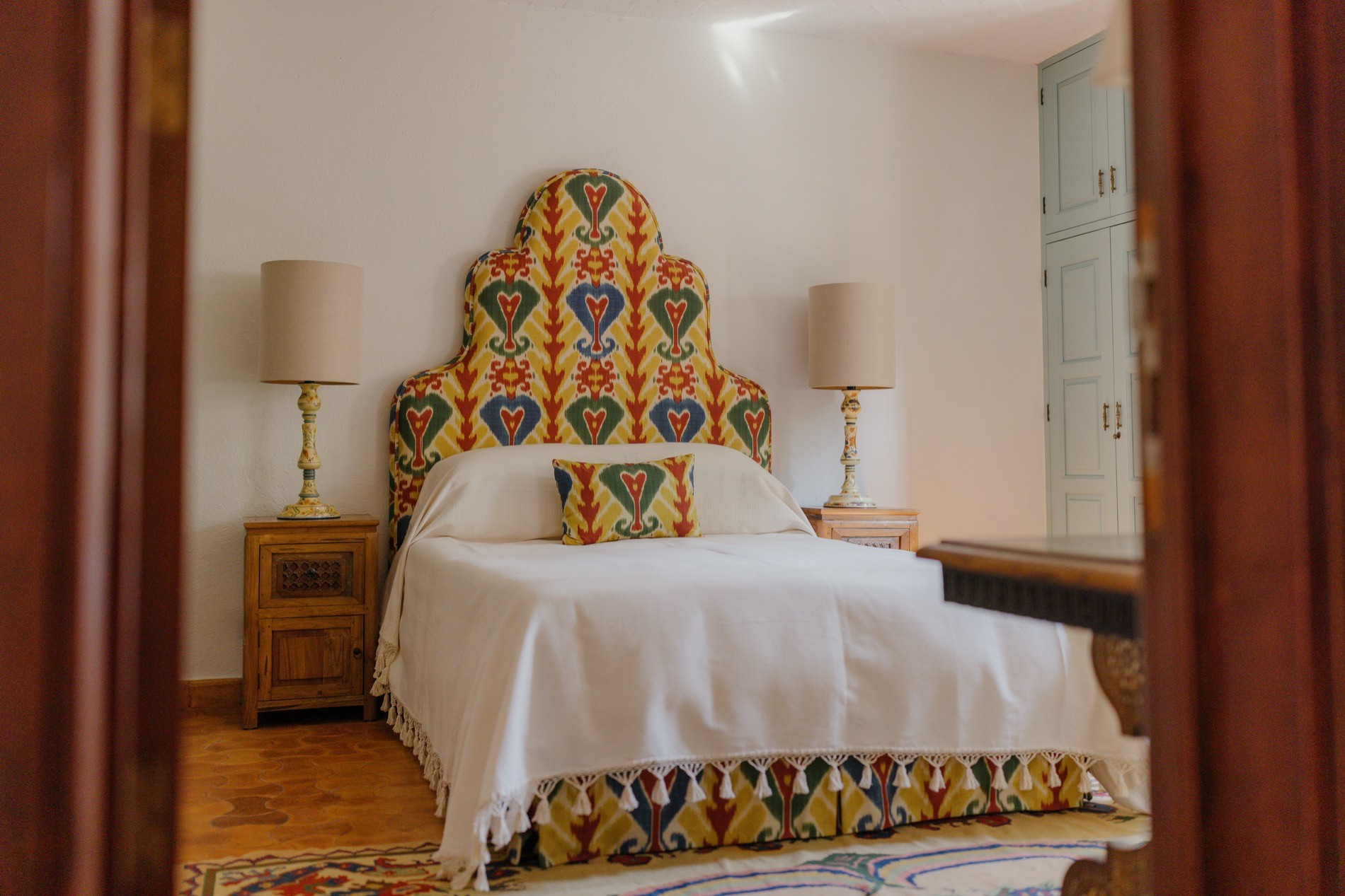 La Residencia guest bedroom with ikat bed, floral needlepoint rug, and whitewashed ceiling