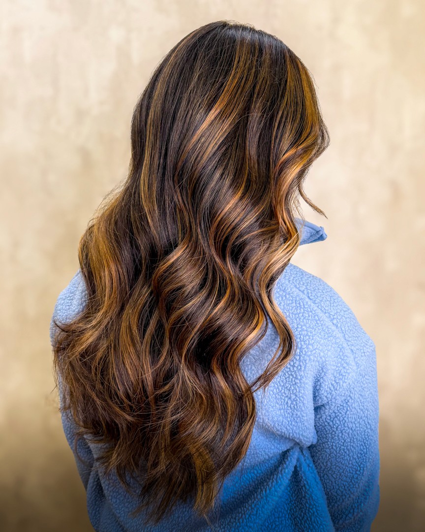 A woman lying down with a towel wrapped around her head, her face glistening with facial oil. Her eyes are closed, and she appears to be enjoying a spa treatment in a peaceful setting.