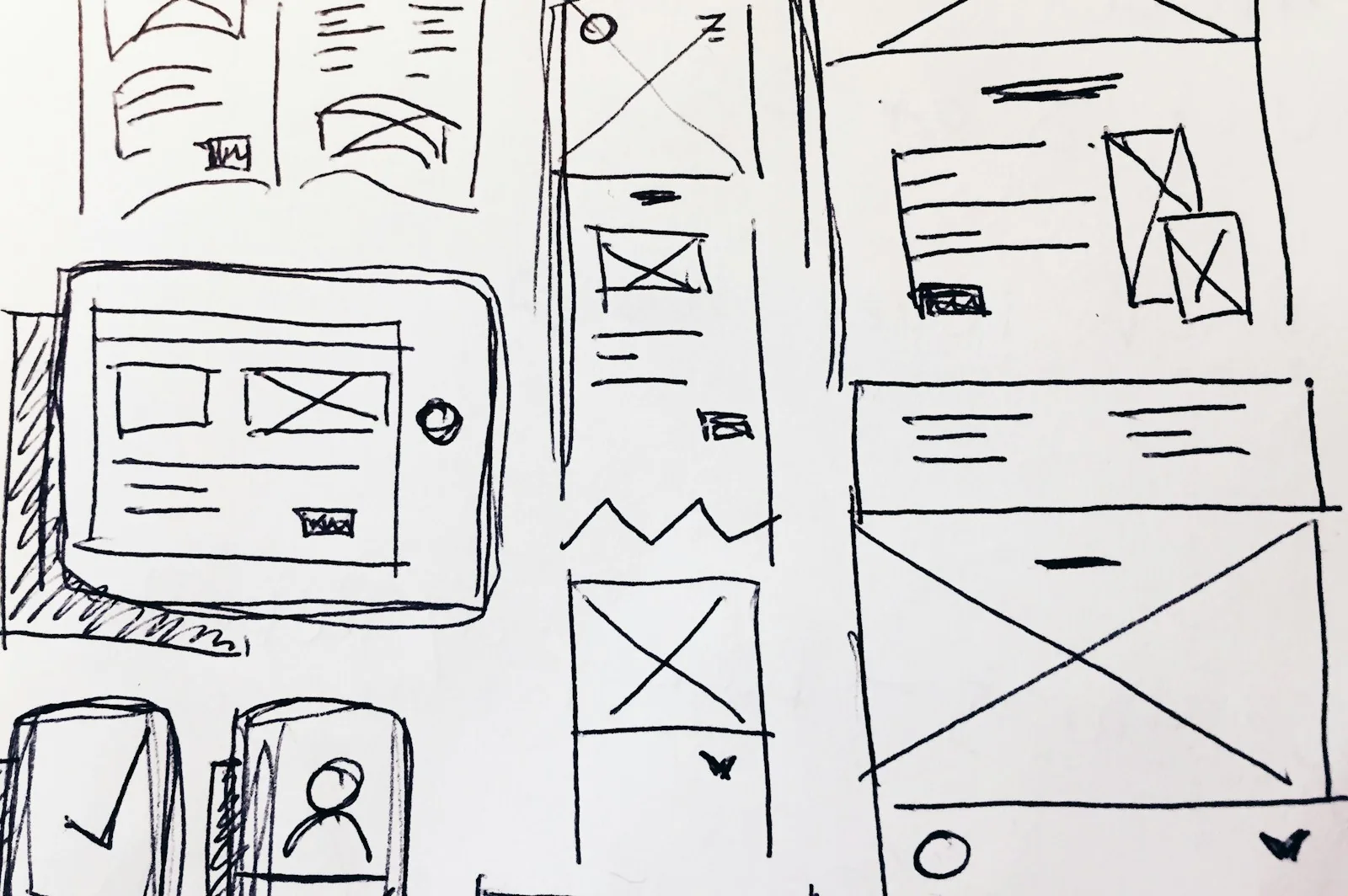 Hand-drawn black ink wireframes of tablet, phone and web page layouts with image placeholders on white paper