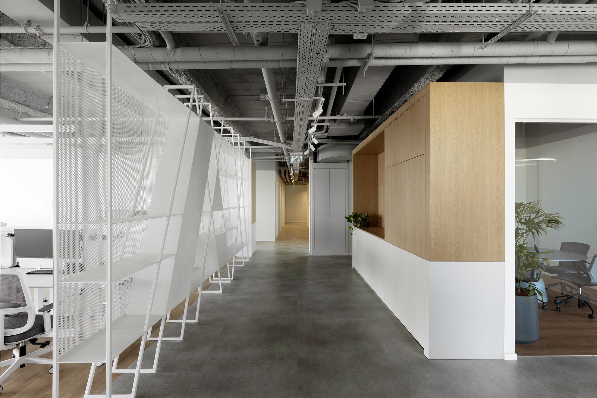 מסדרון ראשי: שילוב הרמוני בין קיר נגרות עץ אלון לאחסון ובין מחיצת רשת מתכת (Expanded Mesh) אוורירית המגדירה את המעבר