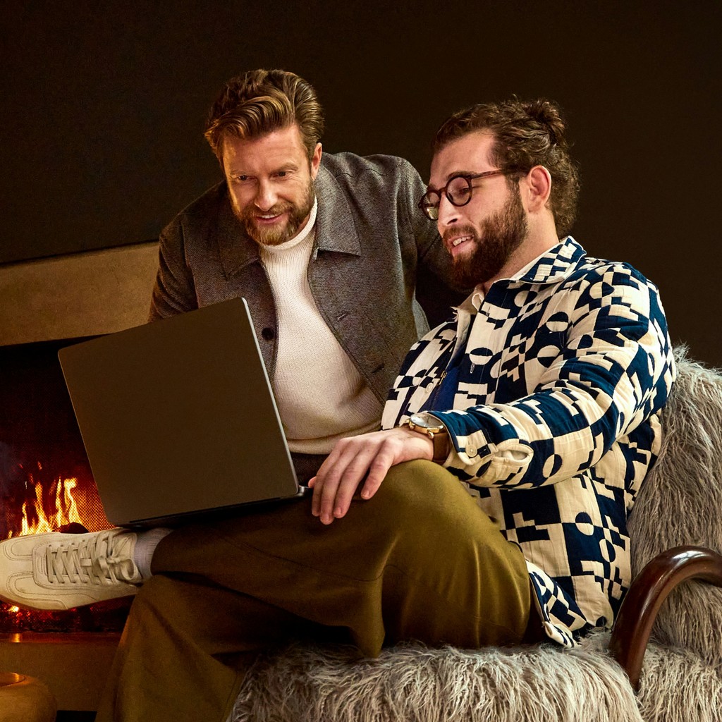 Two men looking at a laptop near a fireplace