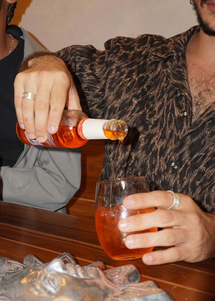 Person wearing silver rings pouring a drink from a bottle into a glass at a bar.