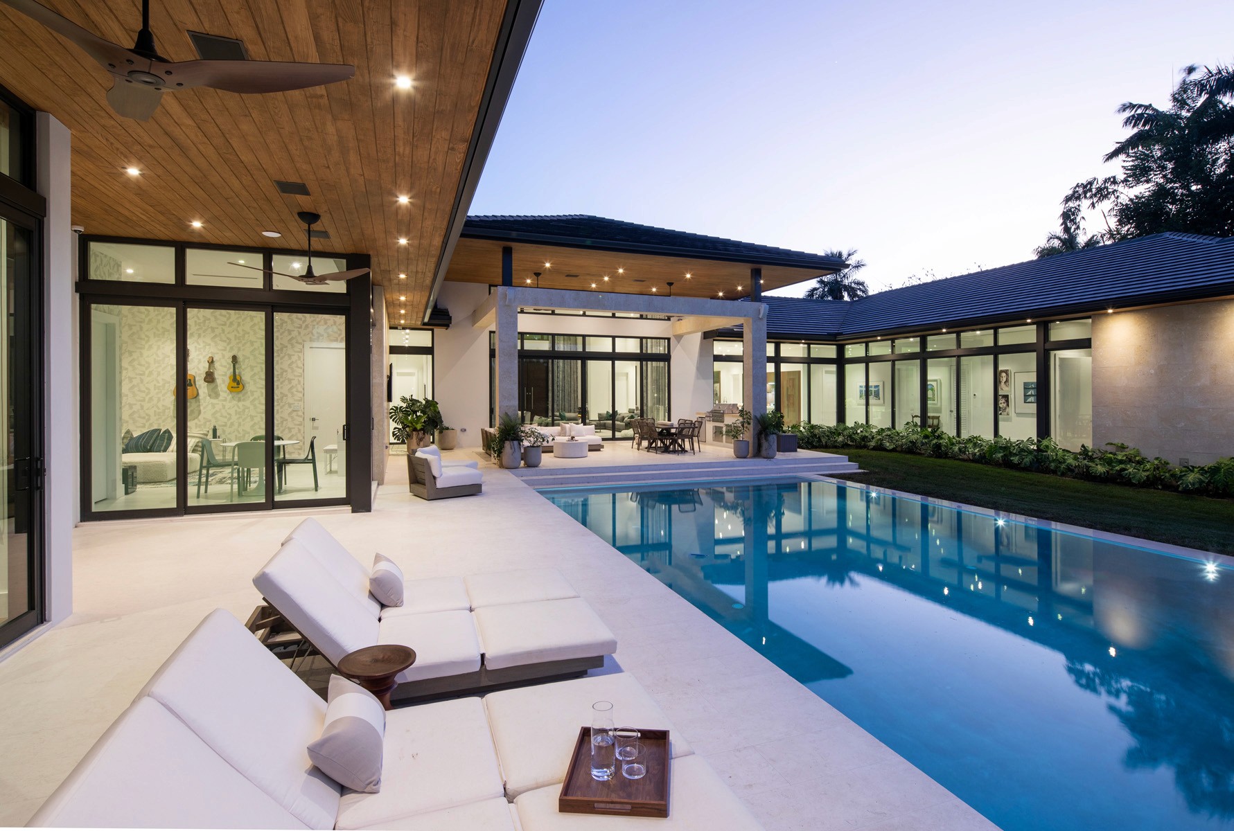 A luxurious custom home in Newport Beach designed by ARCA Builders, featuring expansive glass doors, outdoor seating area, and a swimming pool surrounded by white lounge chairs.
