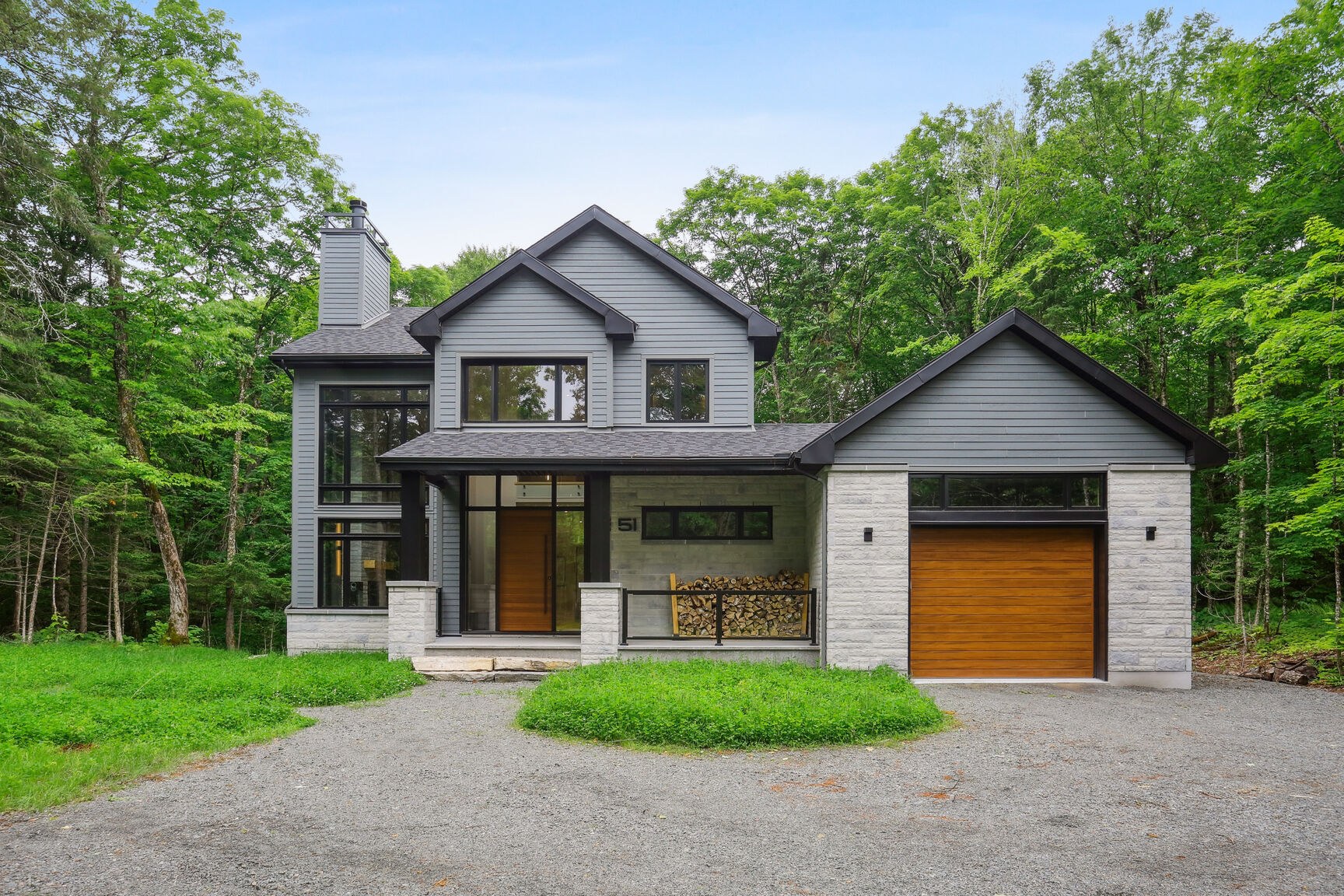 Façade avant et allée de gravier, maison contemporaine en milieu boisé.
