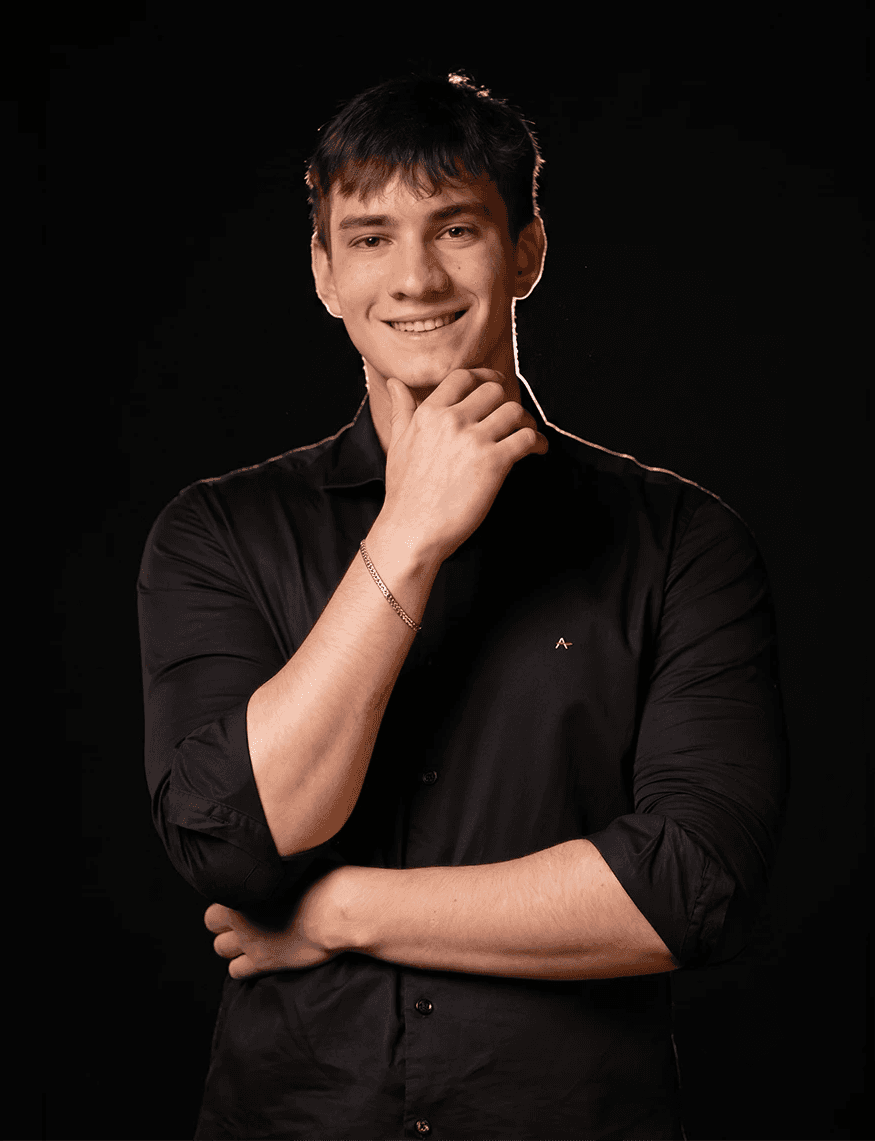 Smiling person with curly hair, wearing a black shirt, against a warm, dark background.