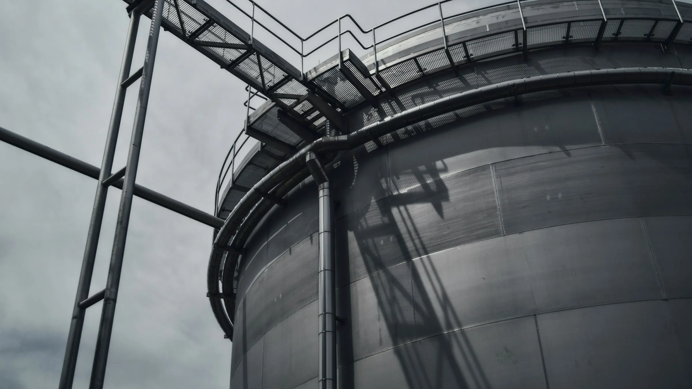A large steel storage tank with an external stairway and walkway, seen from below