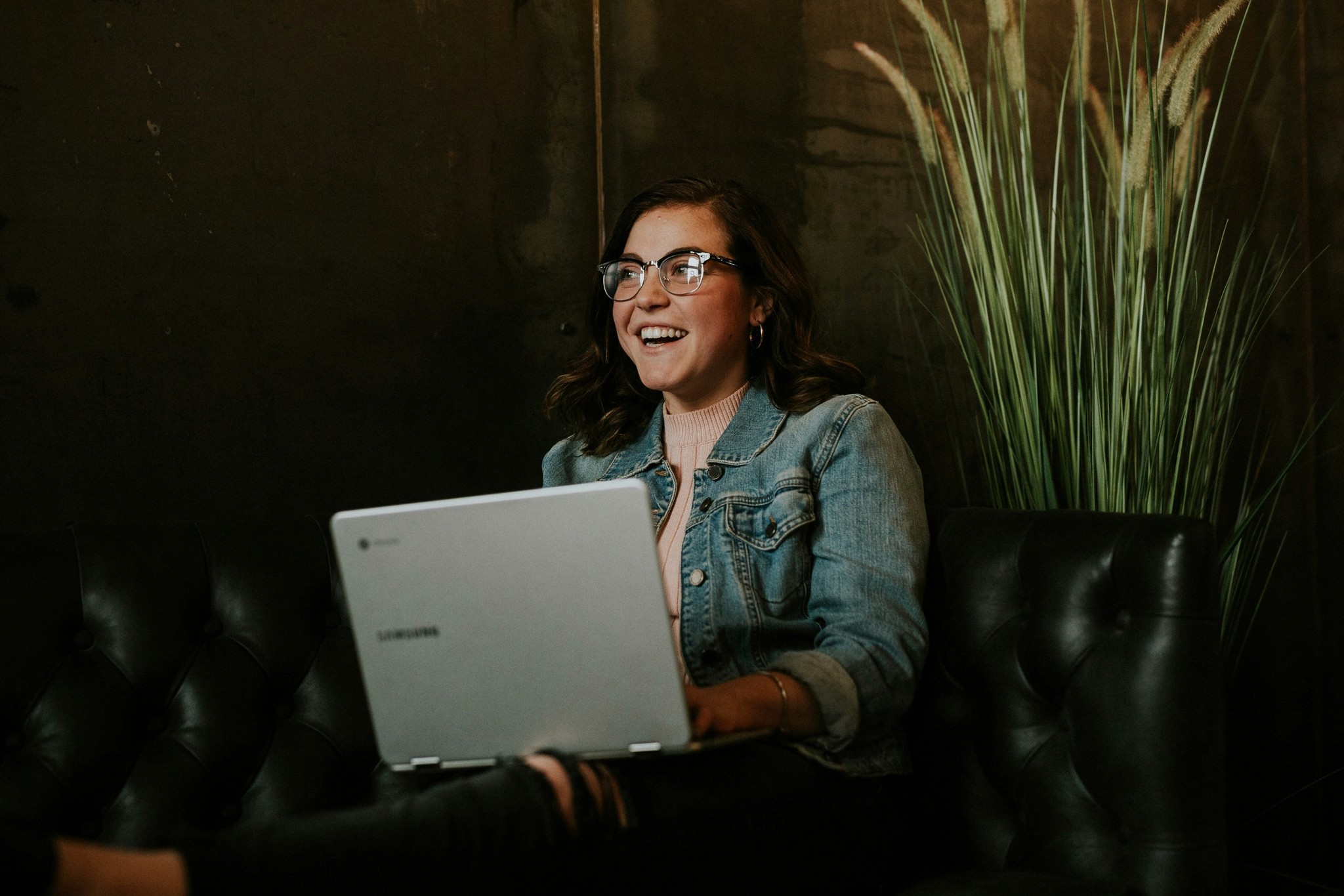 Frau sitzt mit Laptop auf dem schoß auf einer Couch.