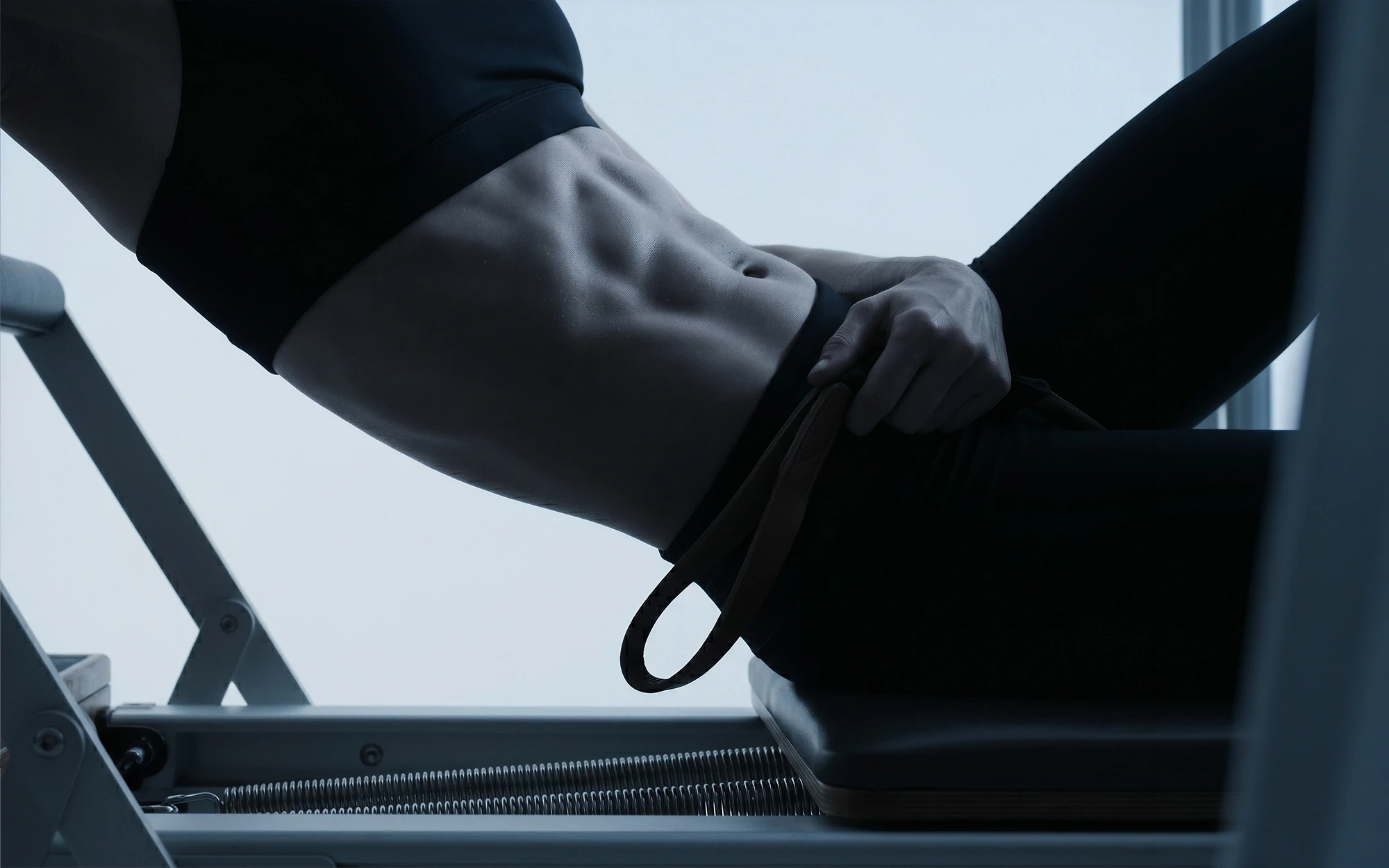 A fit woman exercising on a Pilates reformer, showcasing toned abs and athletic form in a modern setting.
