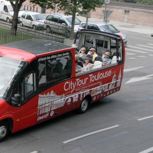 Um ônibus vermelho do City Tour Toulouse com passageiros sentados no deck superior aberto, percorrendo uma rua urbana.