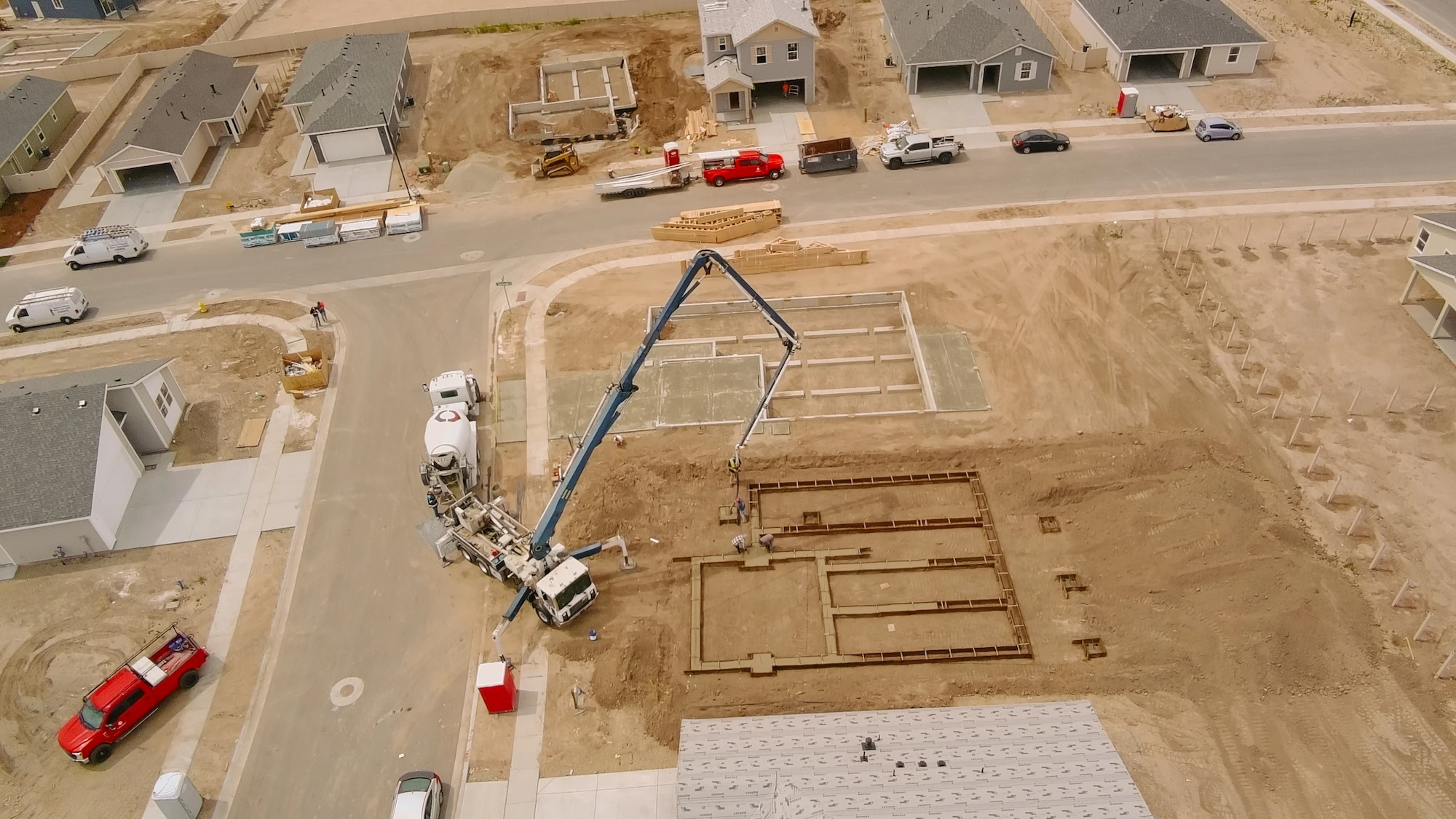 Aerial view of a residential construction site where a concrete pump truck extends its boom over a home foundation.