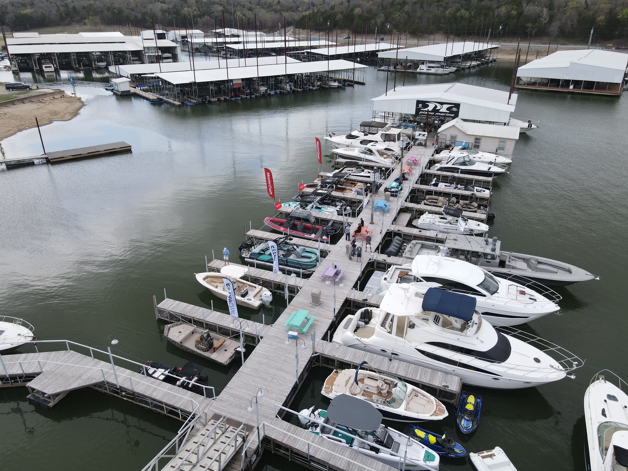 A vibrant marina showcases numerous luxury yachts and boats docked along a wooden pier, surrounded by calm water and adjacent to covered docking areas.