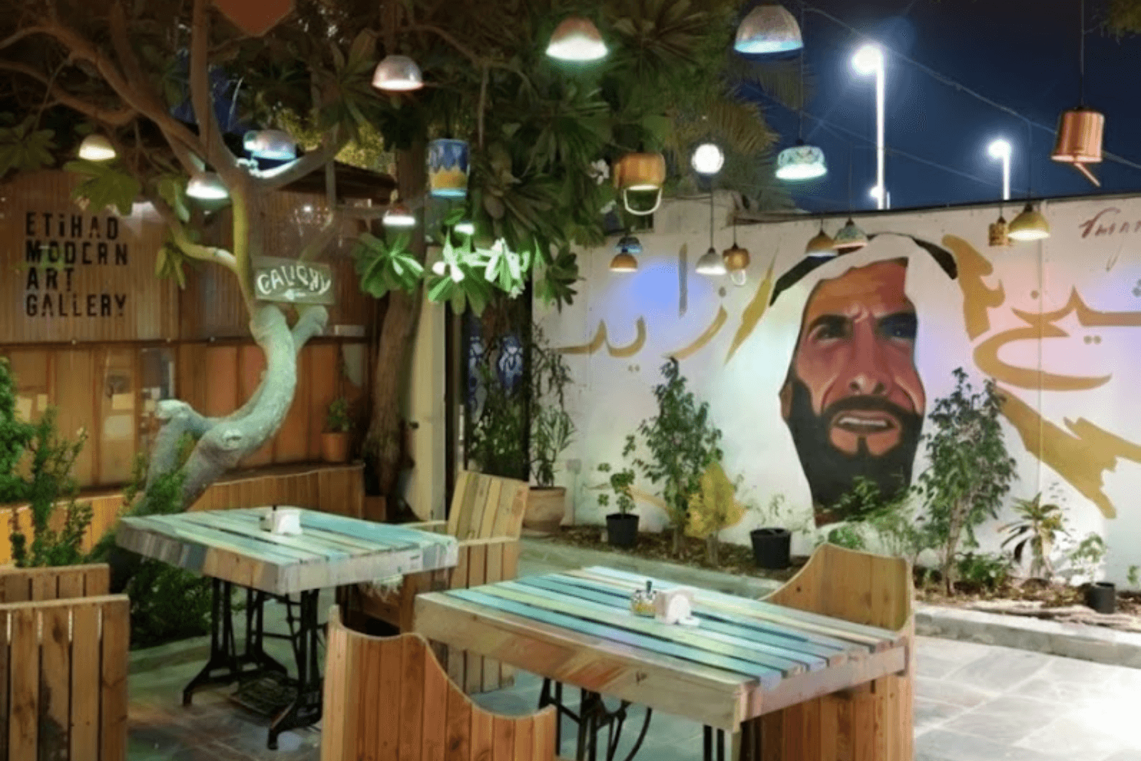 Artistic outdoor cafe space with painted hanging mugs and a mural at Art House Café in Abu Dhabi.