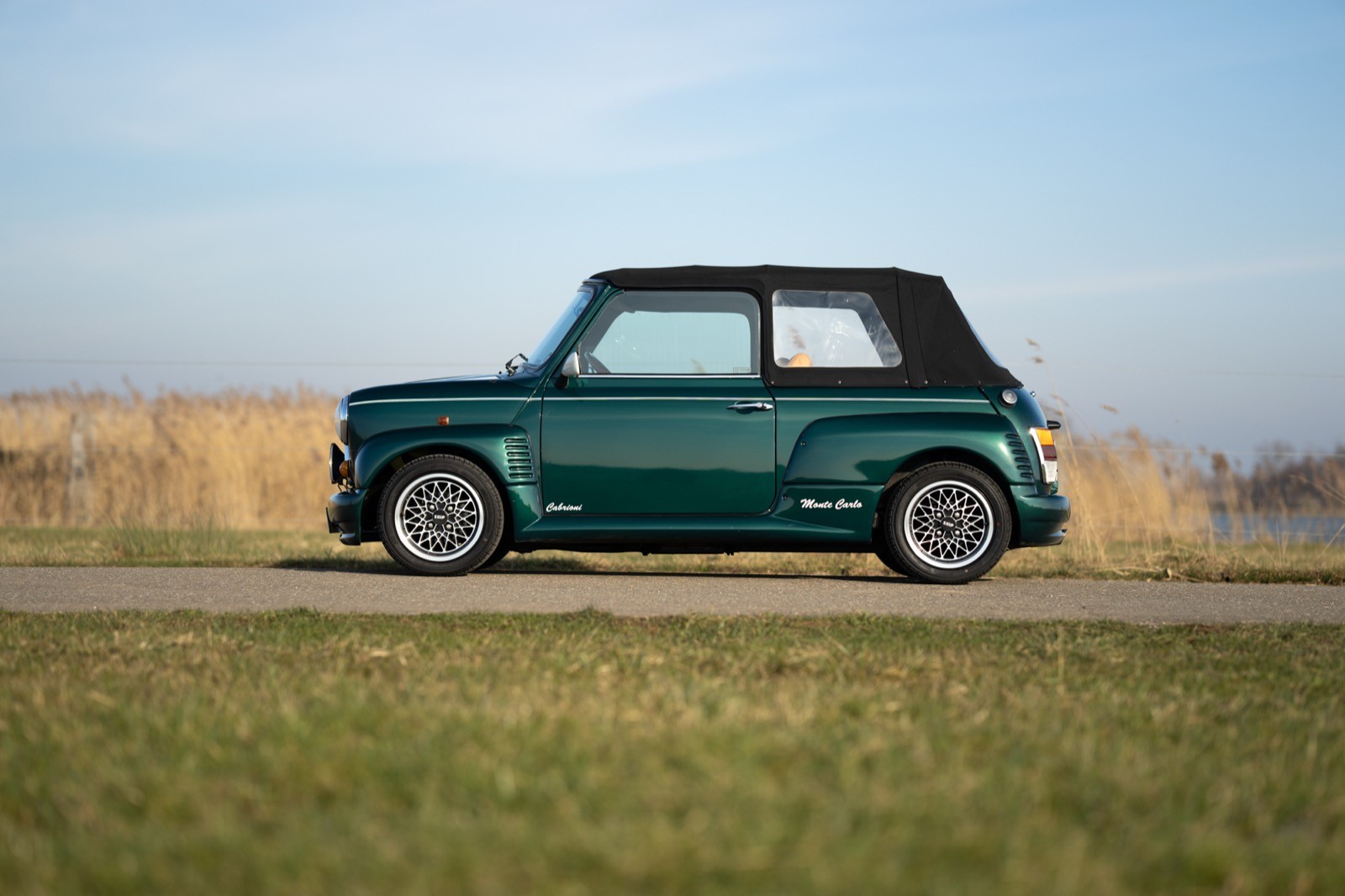 A classic green convertible car parked on a grassy area with a clear blue sky in the background.
