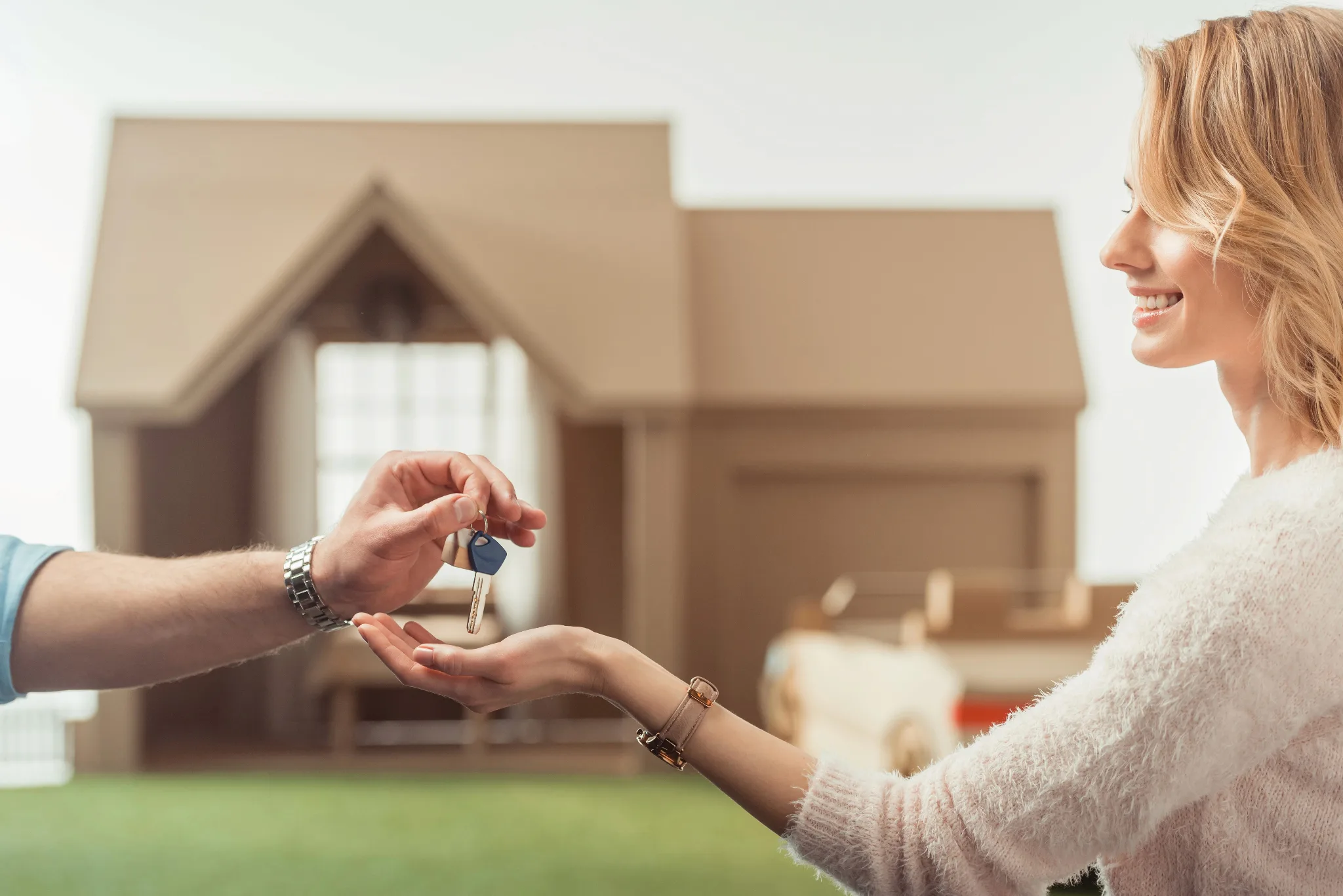 Caucasian woman being handed house key, with a house in out-of-focus in the background.