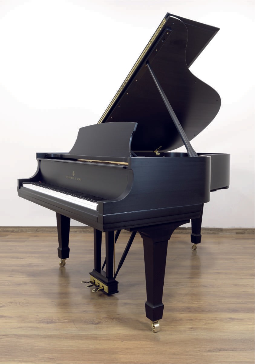 A fully restored Steinway & Sons grand piano in a satin ebony finish, displayed in a bright showroom.