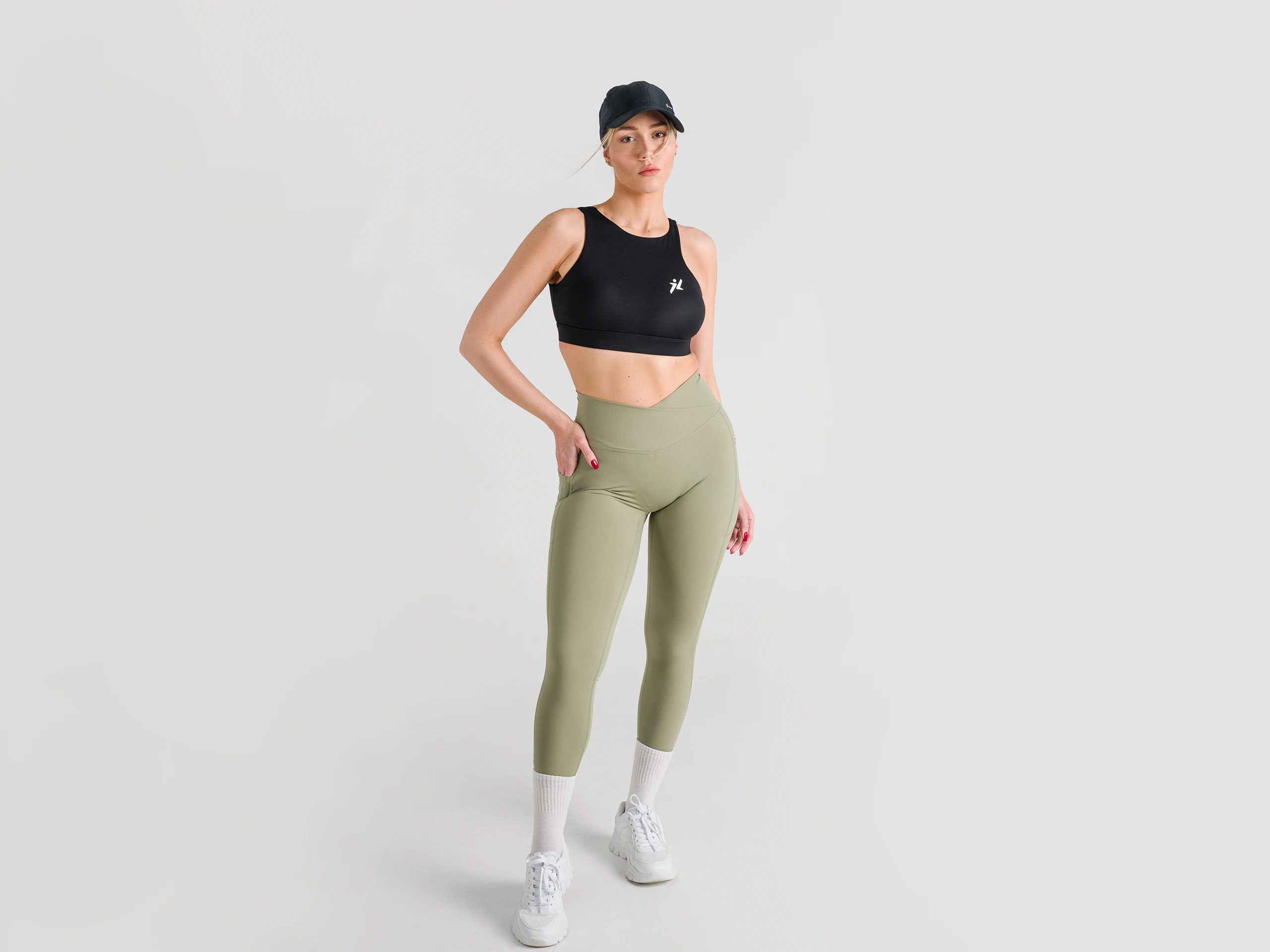 Confident woman in black sports bra and green leggings posing in a minimalist studio.