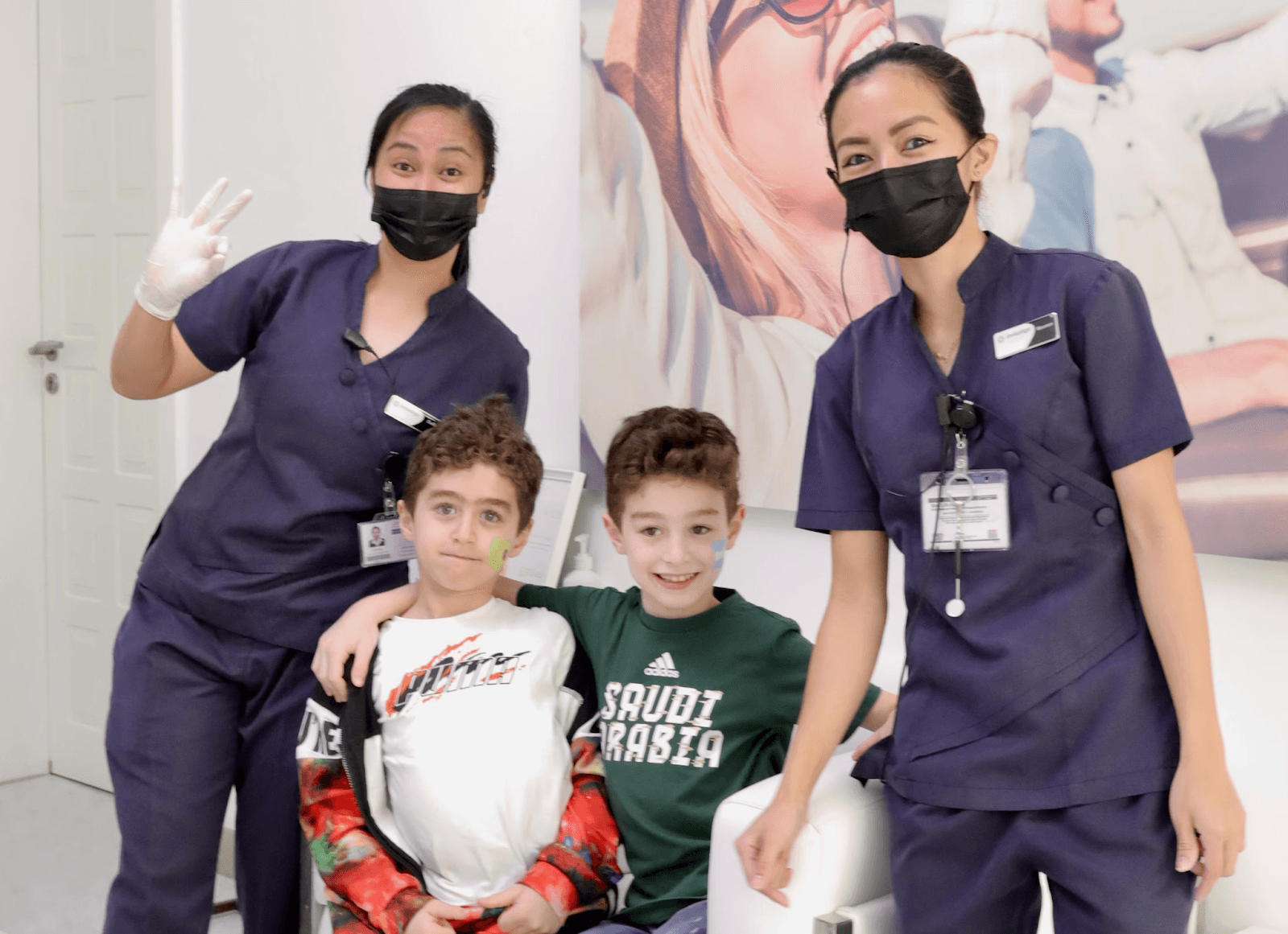 لقطة تظهر دكتور أسنان أطفال بجانبه أطفال سعداء في عيادة أسنان أطفال انفزلاين.