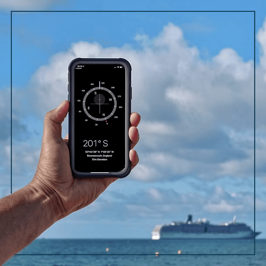 Hand mit Handy und Kompassapp, ein Schiff im Hintegrund