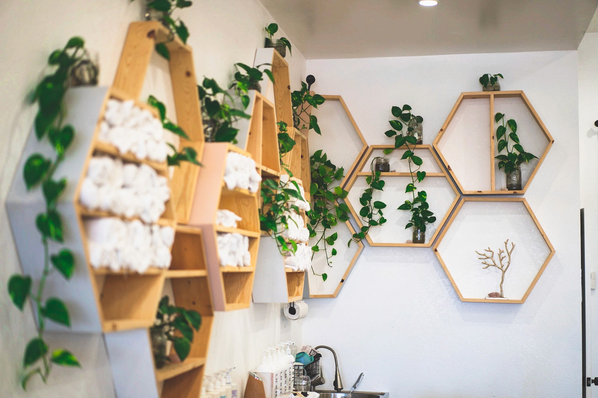 Wall-mounted octagon towel shelves at Del Sol Hair Studio, styled with rolled white towels and greenery for a clean, modern, and inviting look.