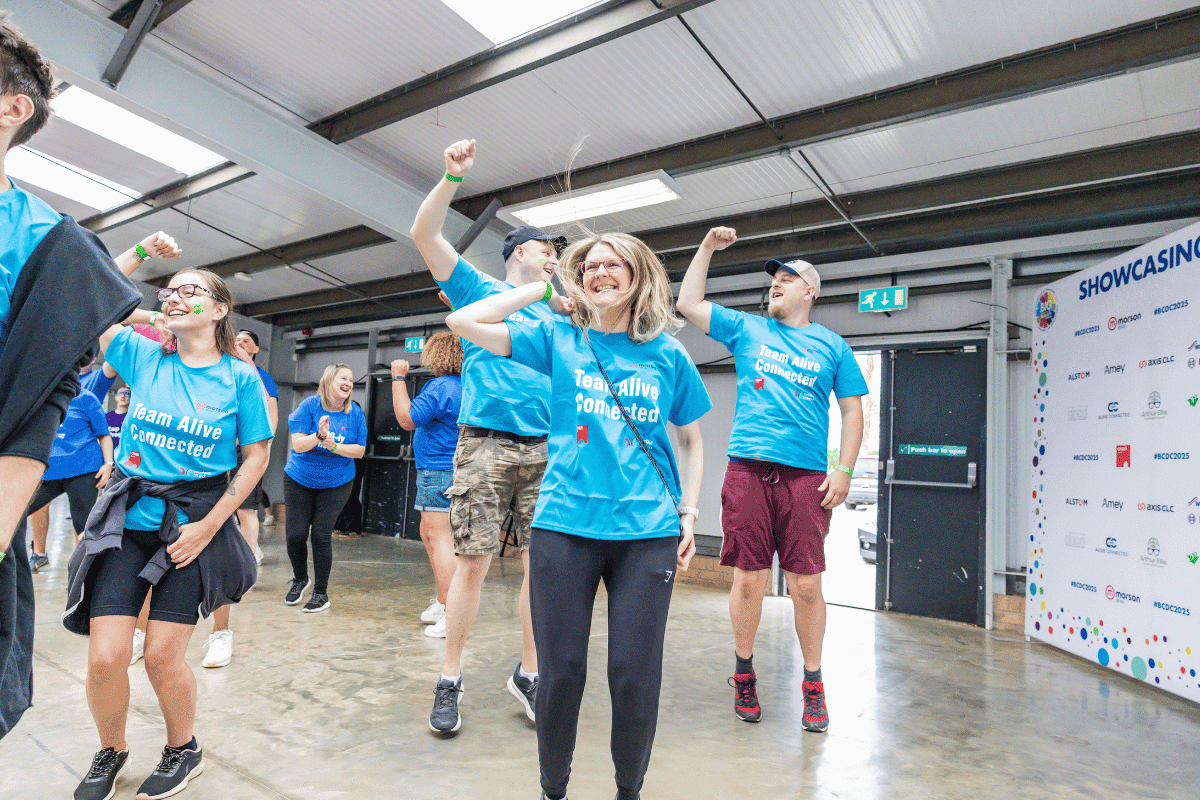 Outdoor team-building event with participants wearing matching blue shirts, taking part in inflatable obstacle courses and games, smiling and cheering, with the words 'ENTER A TEAM' in large bold white and green text across the image.