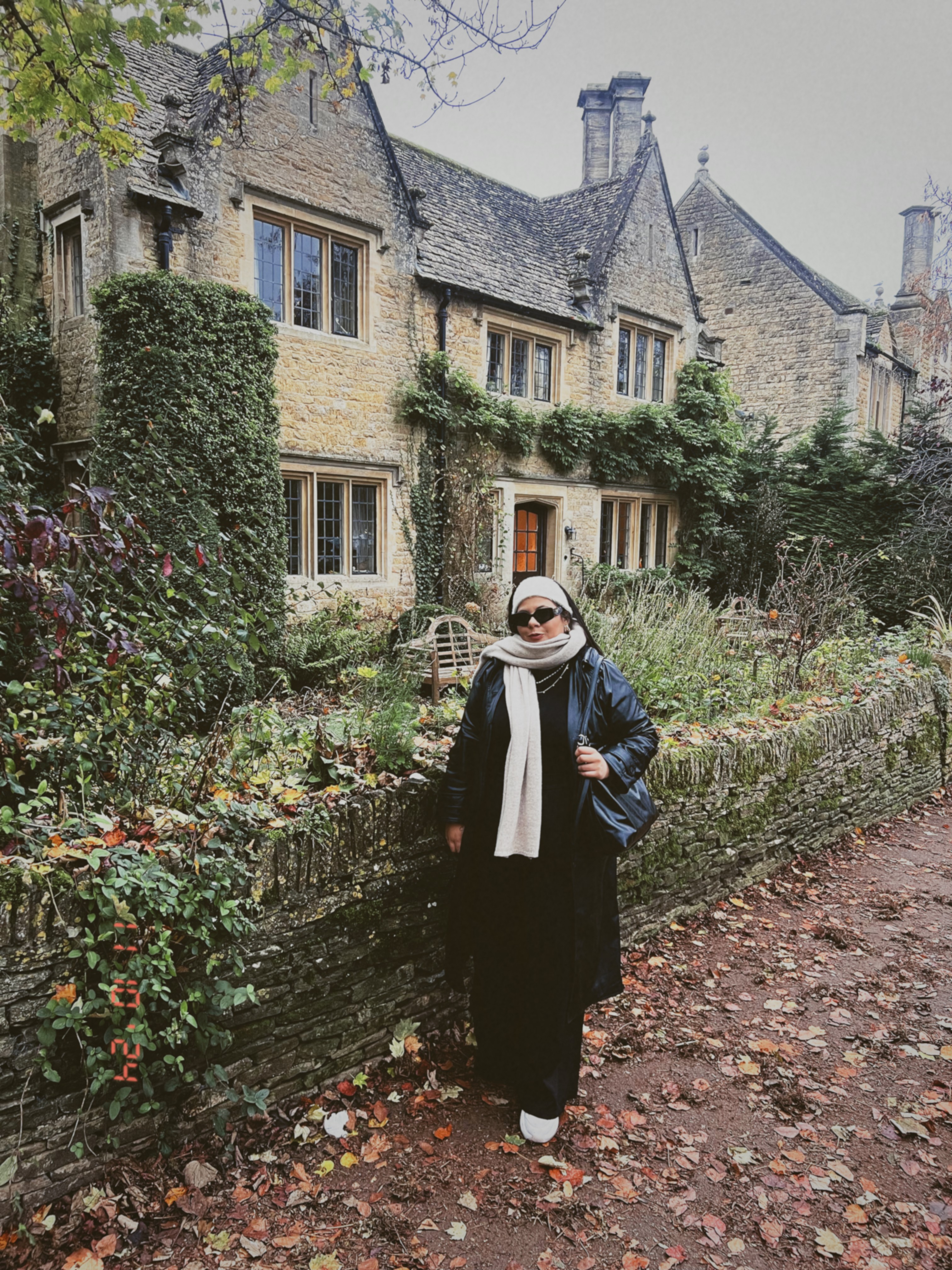 A young person with curly hair smiles at the camera while sitting in front of a laptop against a dark background.