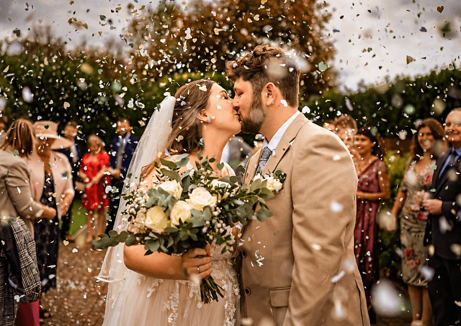 A bride in a white lace wedding dress holds a colorful bouquet of pink, yellow, and orange flowers.