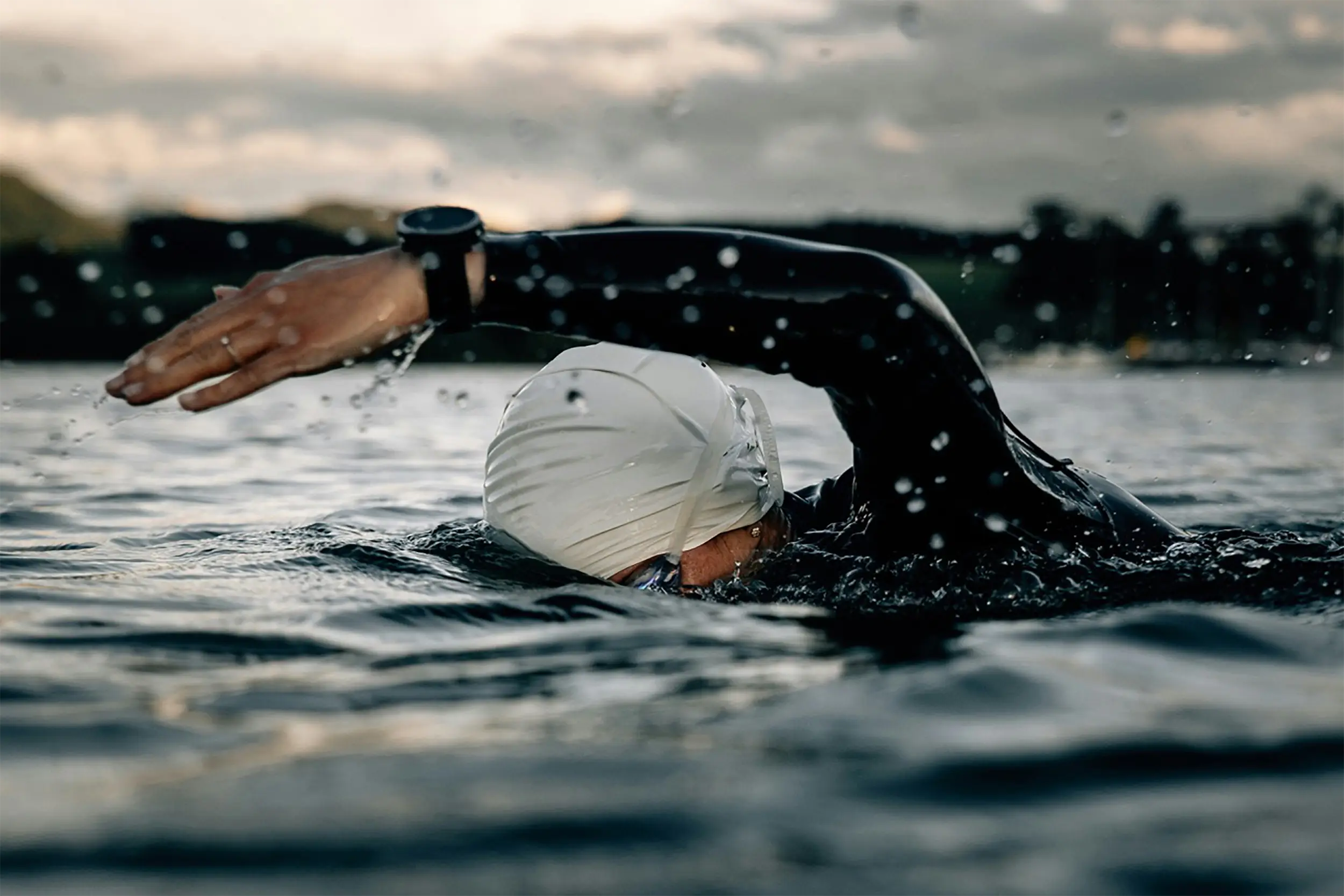 Well-Fit Ironman coach client swimming open water in a wetsuit during an early morning triathlon training session