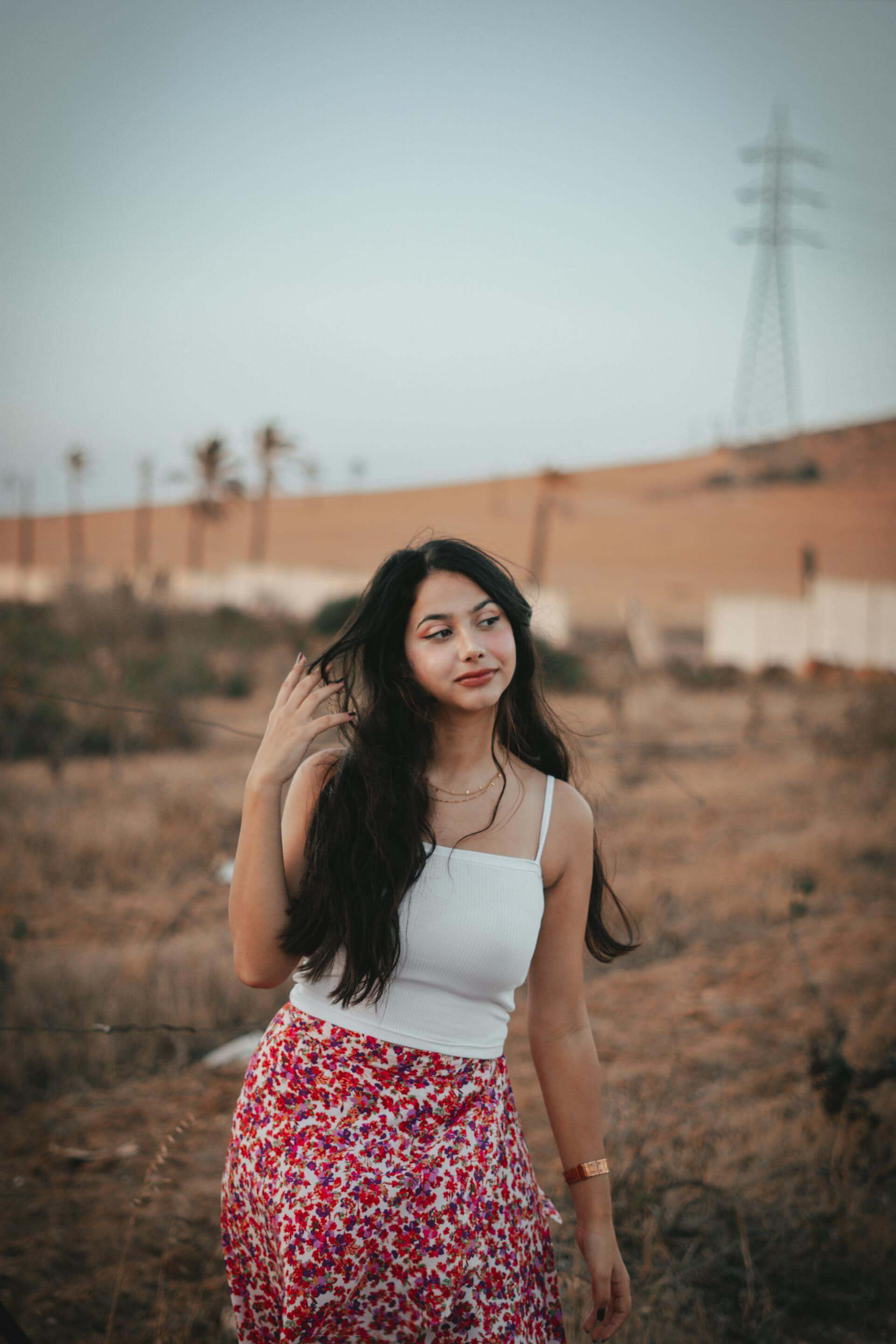 A woman in a floral skirt stands gracefully in a vast desert landscape under a clear blue sky