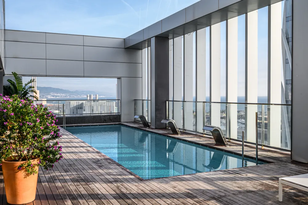 Modern commercial rooftop pool with glass fencing and city views in the background.