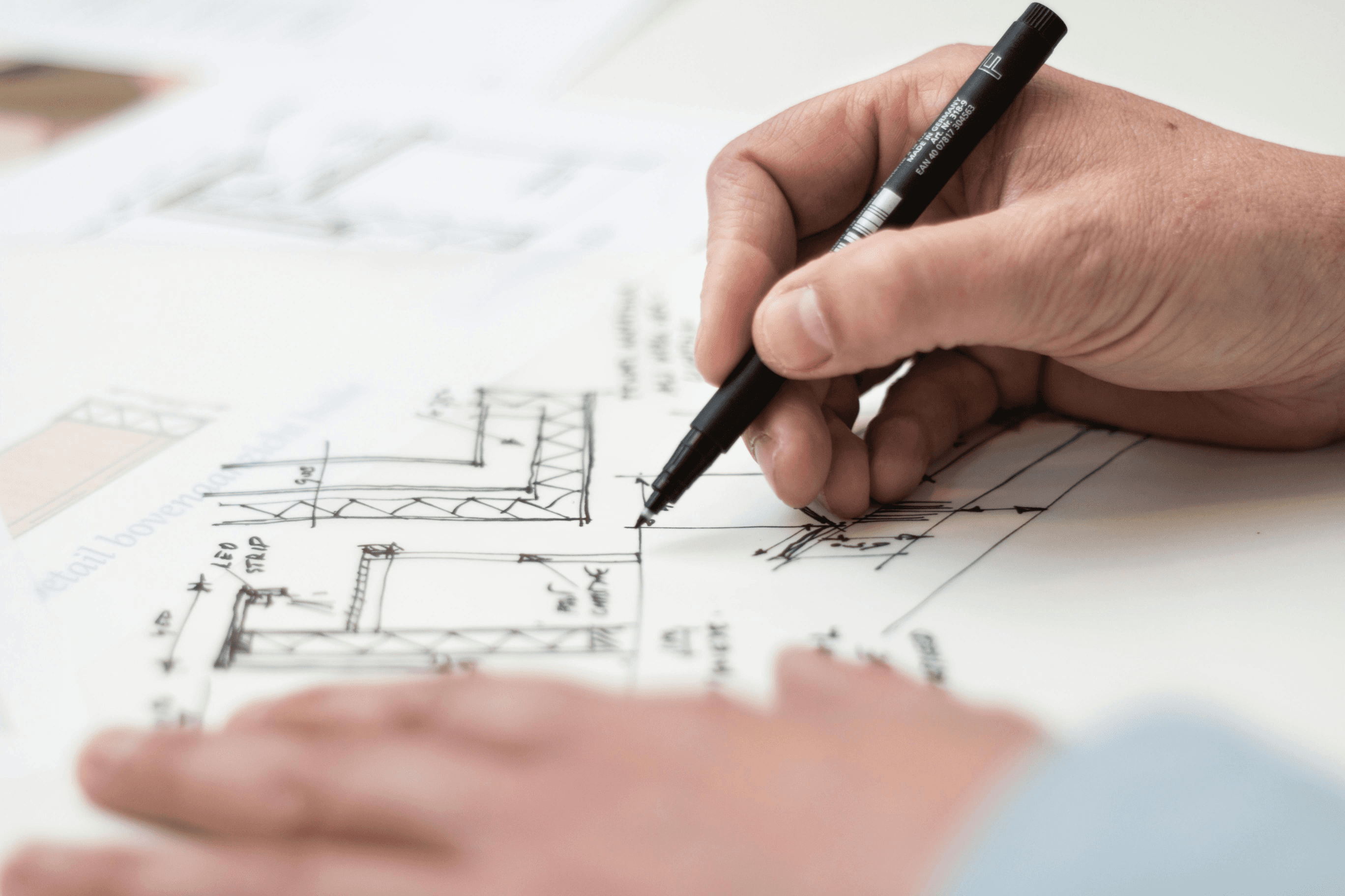 Architect drafting detailed building plans with pen on paper.