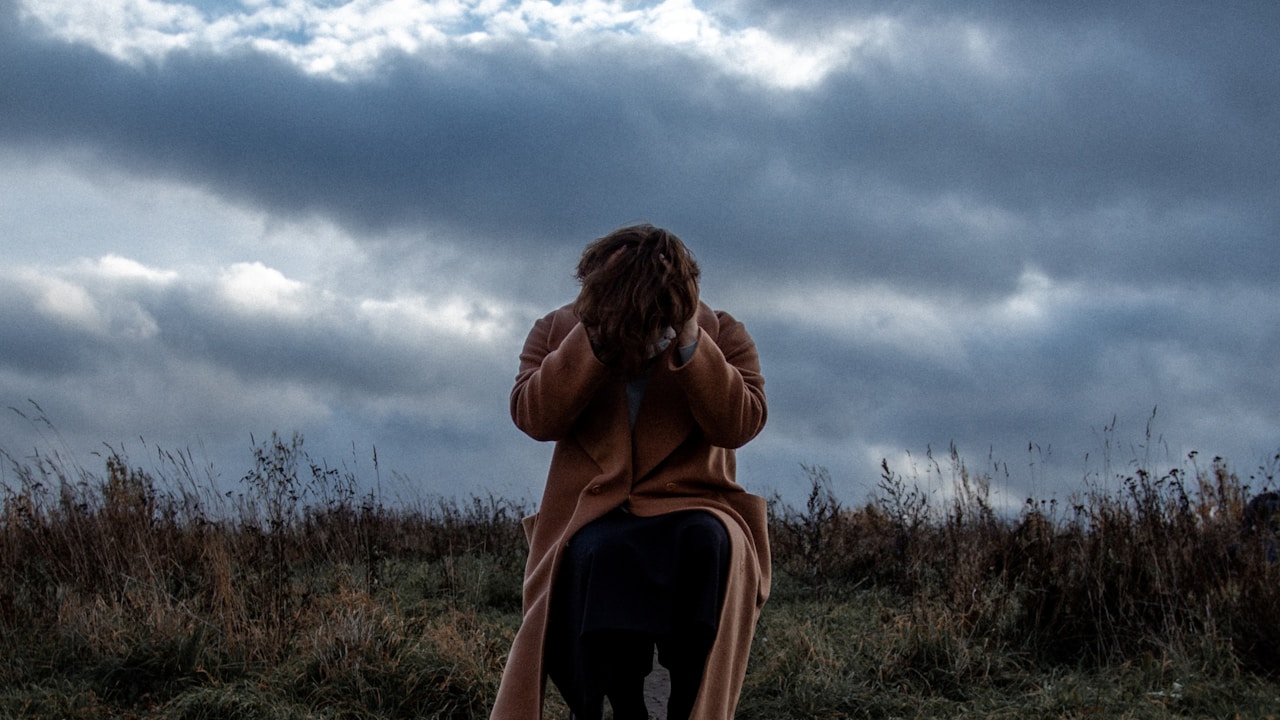 Person sitting alone in a field feeling overwhelmed by existential thoughts | Photo by Andrey Tarasenko on Unsplash