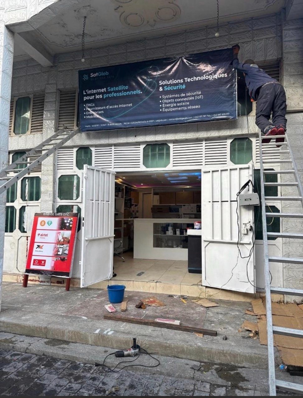 Worker installing a SatGlob satellite internet signage on a building facade in the DRC as part of Bridge Sats' enterprise connectivity project