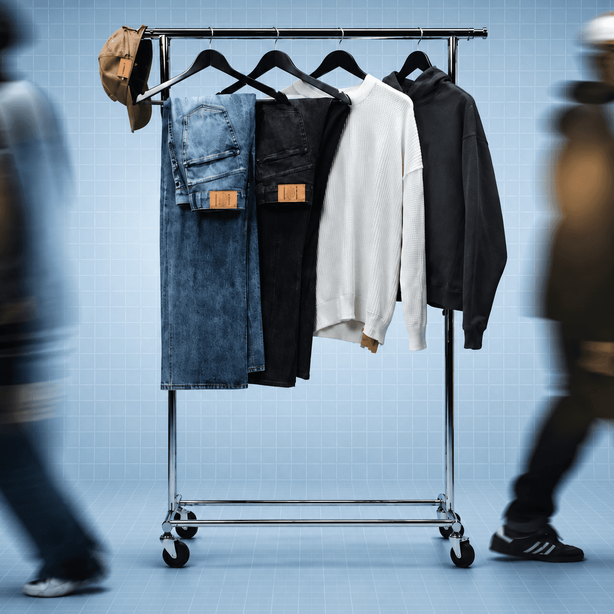 Blue Rewards fashion campaign thumbnail showing a clothing rack with jeans, knitwear, and a hoodie against a light blue grid background with blurred pedestrians in motion.