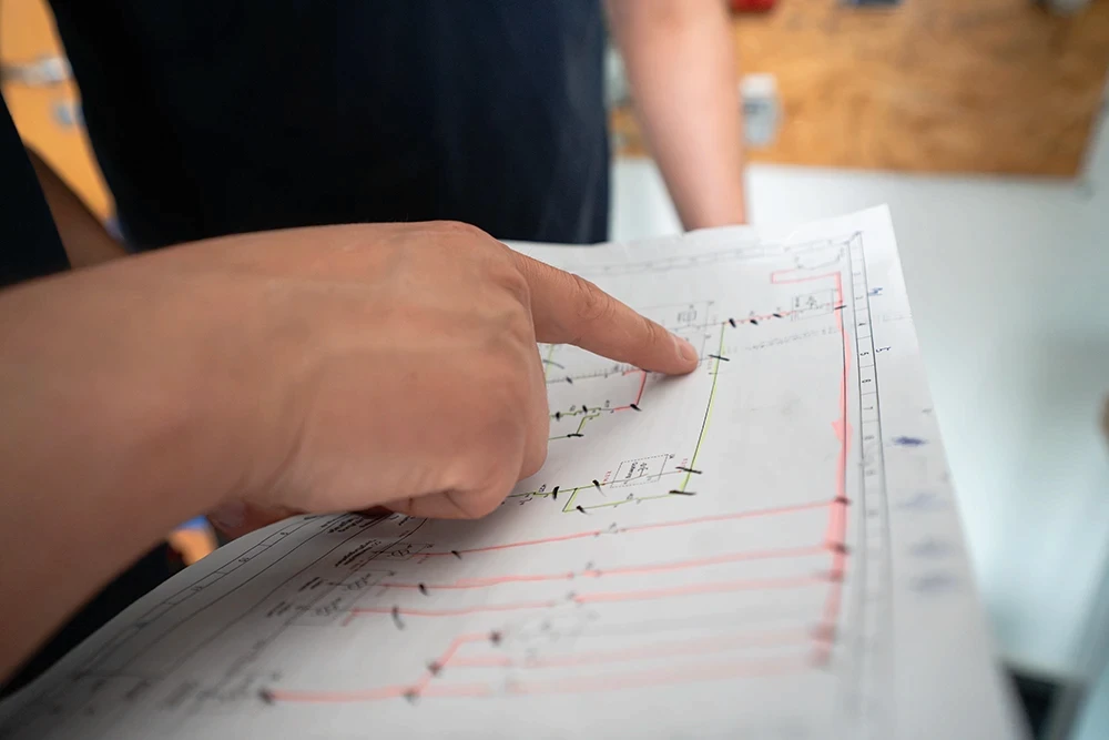 Eine Hand zeigt auf einen Elektroleitplan, während zwei Mitarbeitende von RITTER Starkstromtechnik die technischen Zeichnungen gemeinsam besprechen. Der Fokus liegt auf der Abstimmung der Elektroplanung.