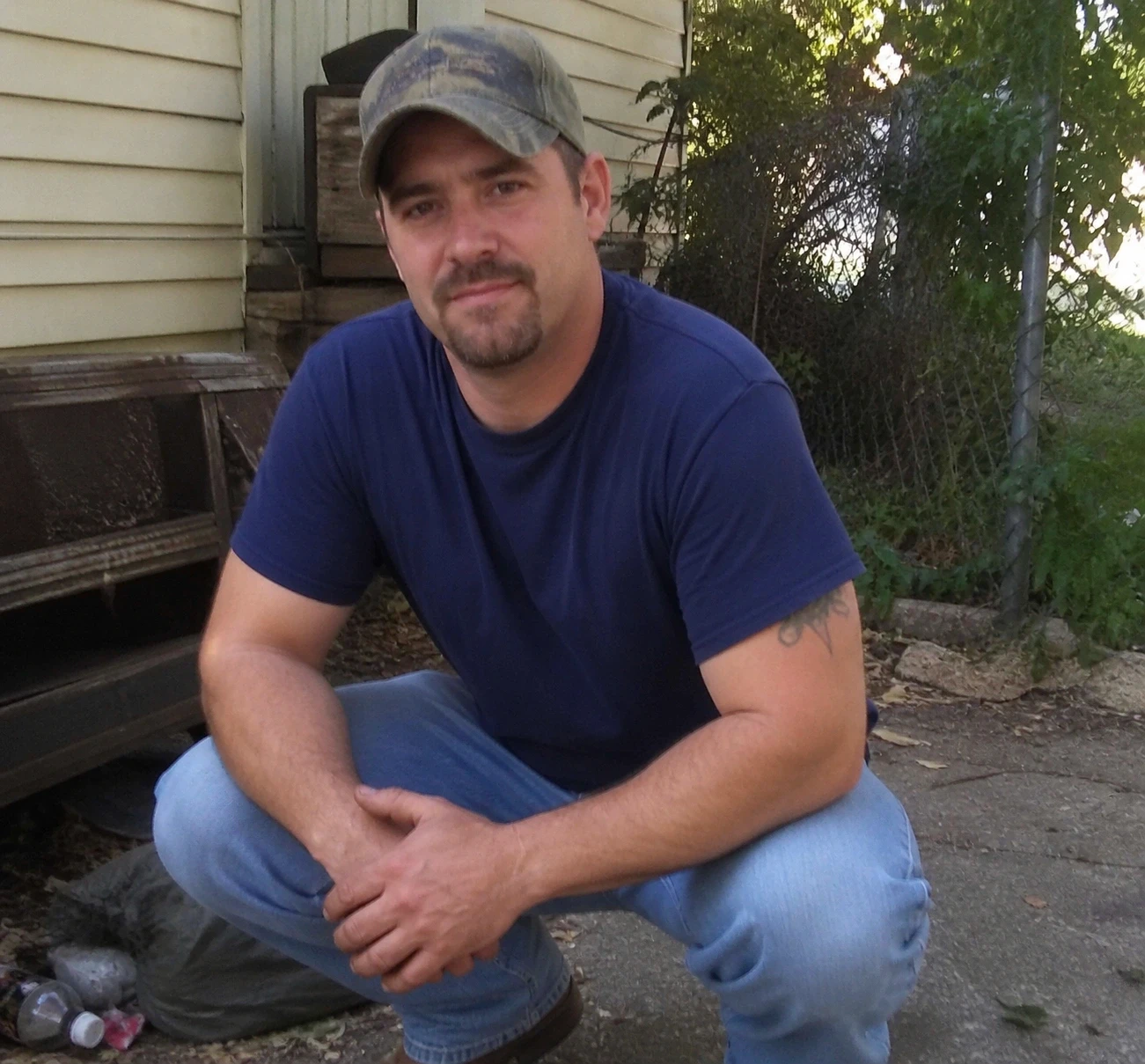 Man in blue shirt and cap crouching outdoors