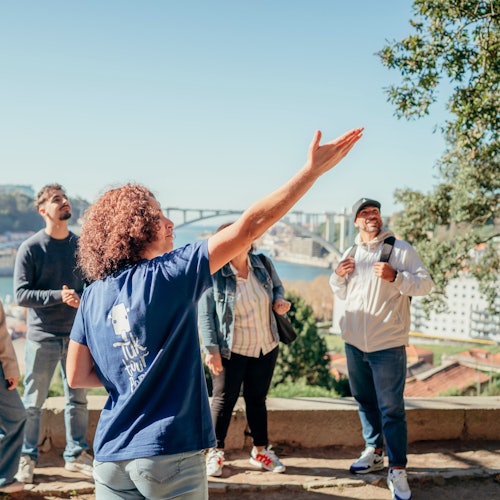 一名女士在户外对五人小组讲话，她身后是一座桥和城市景观。