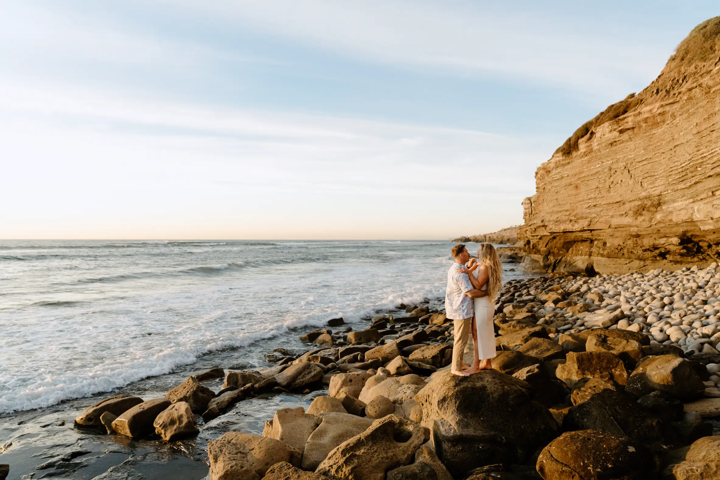 A serene coastal view with rocky shorelines and gentle waves under a clear sky, located at Sunset Cliffs in San Diego, California.