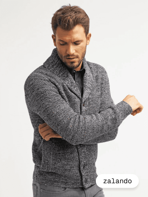 A smiling woman with her arms crossed, standing against a dark green background. She has long, dark hair.