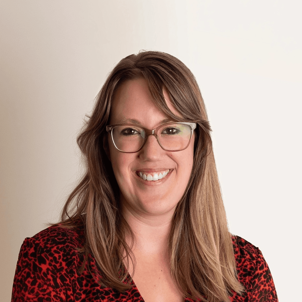 Vrouw in een opvallend shirt met geometrisch patroon, lid van het supportteam van Kader Qnect, poseert voor een neutrale achtergrond.