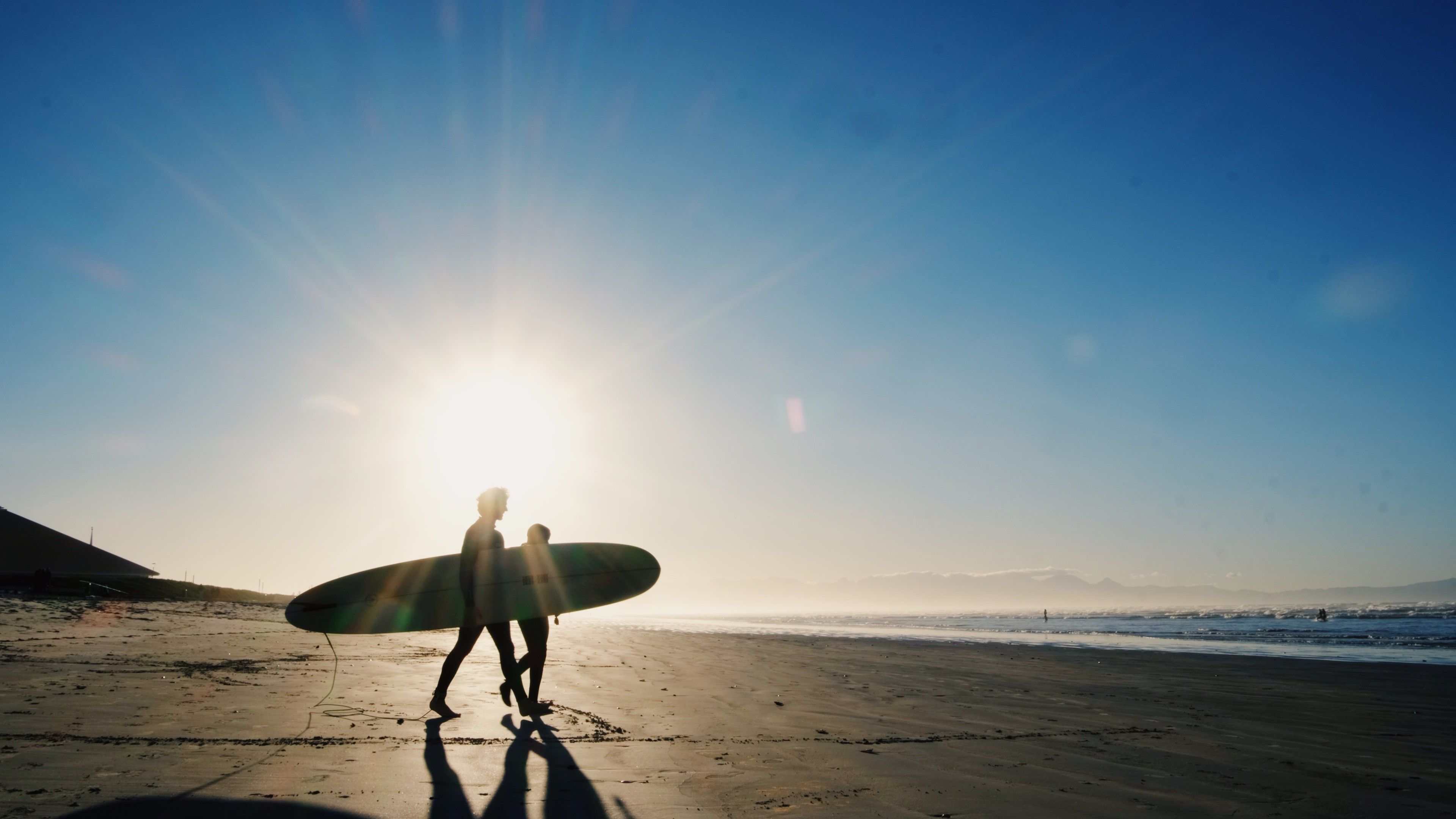 A beginner surfer heading to the ocean with his surf coach to start his surf lesson in Muizenberg, Cape Town