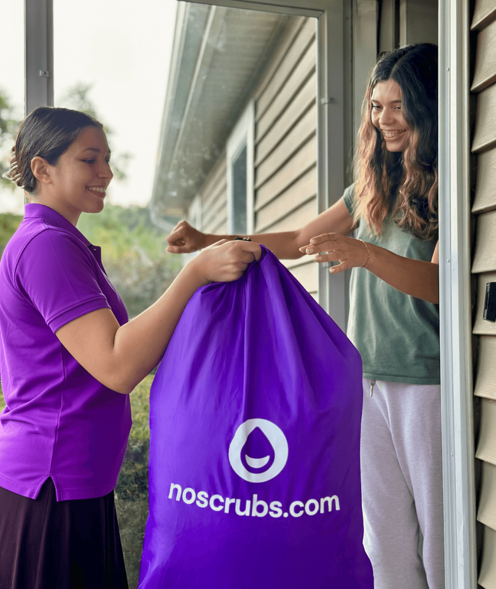 A NoScrubs Scrubber handing a laundry bag of clean clothes to a customer at her doorstep.