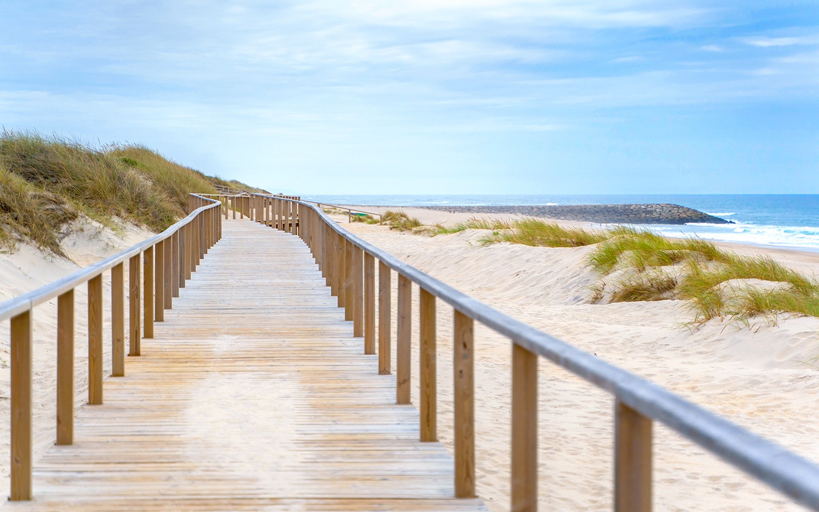 Wooden boardwalk leading to sandy beach in Aveiro, Portugal, with ocean view.