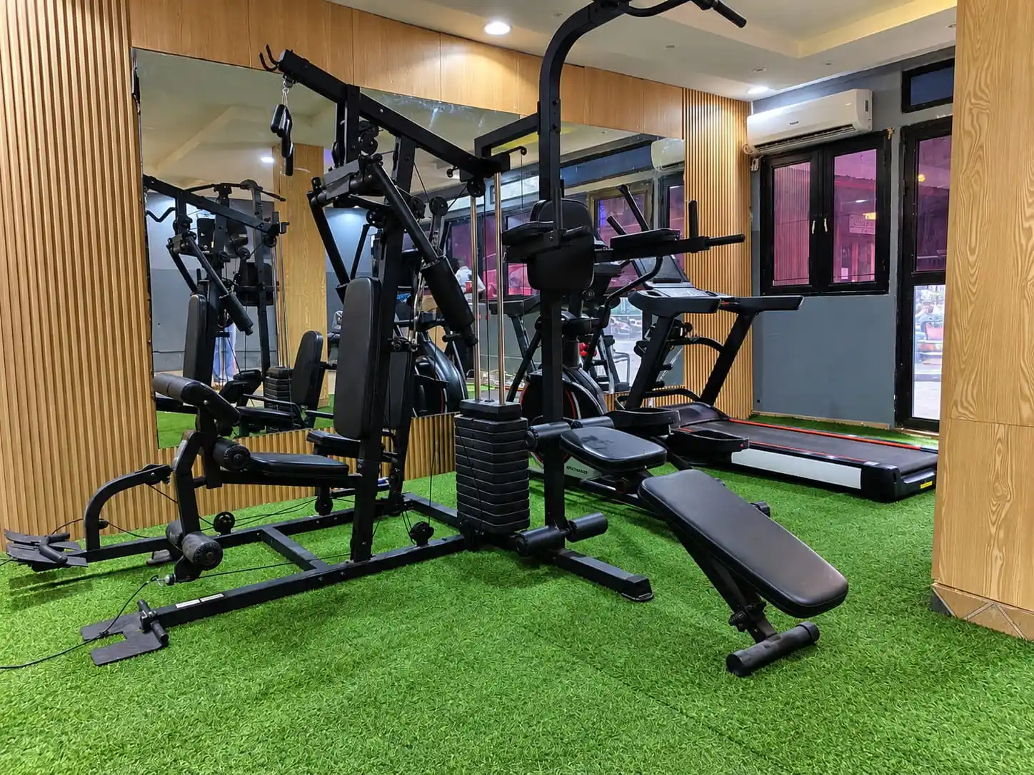 Appareil de musculation multifonction et banc dans la salle de sport, avec tapis de course en arrière-plan.