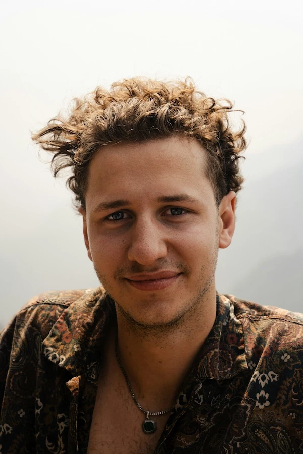 headshot of a young, brown curly-haired man
