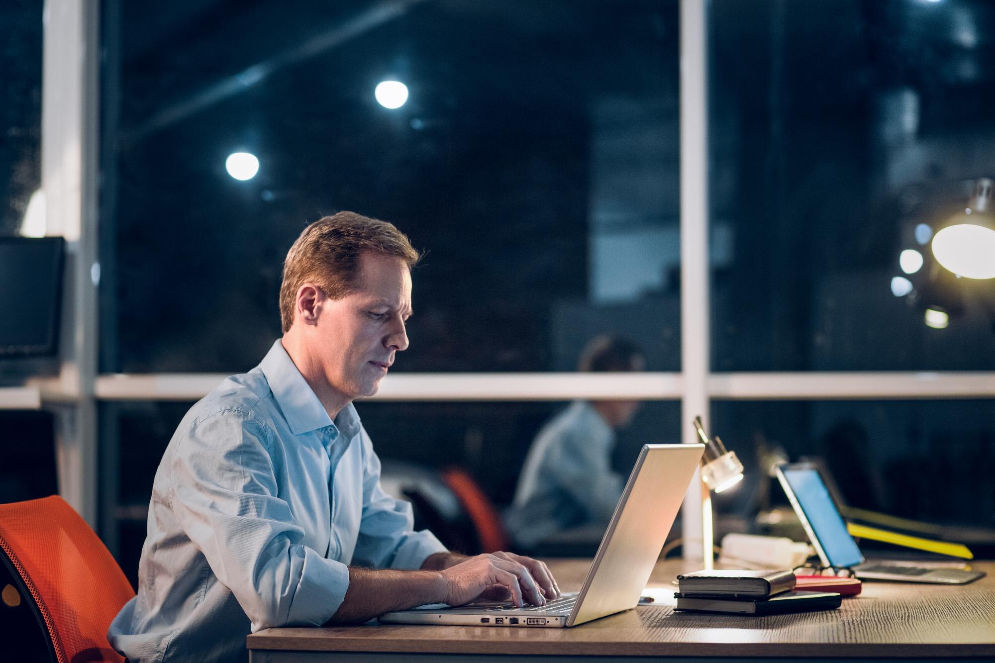 Ondernemer werkt 's avonds aan laptop in modern kantoor