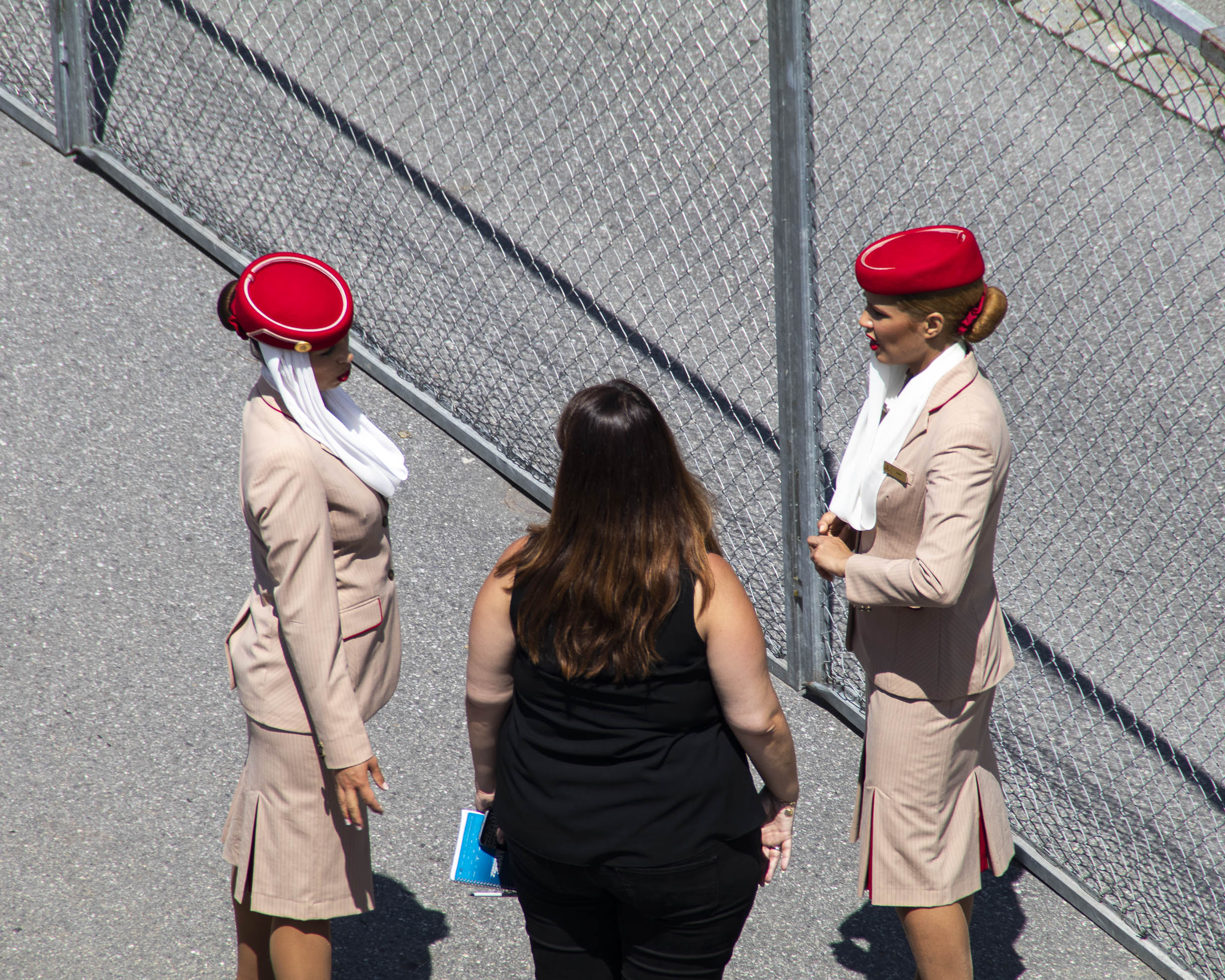 Trois femmes discutant entre elles dont 2 sont des hôtesses de la compagnie aérienne Qatar Airways habillées en tenues d'hôtesse de l'air et la troisième femme légèrement en surpoids porte un débardeur noir